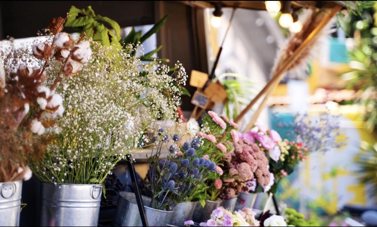 Colorful array of flowers in metal buckets at a market stall.