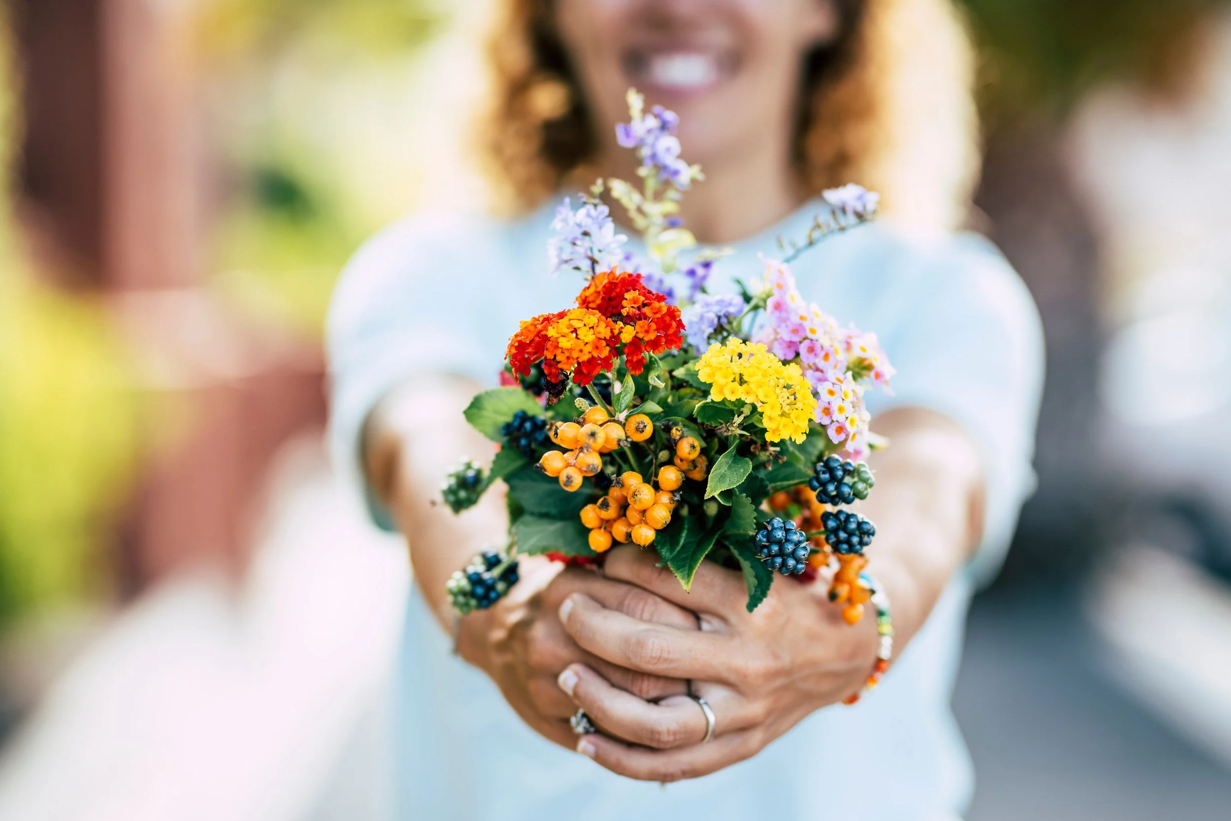 Person holding a colorful bouquet of flowers and berries, smiling with a blurred background.