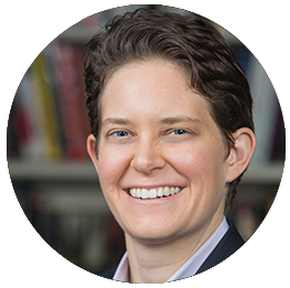 A smiling woman with short dark hair in a library or bookstore setting.