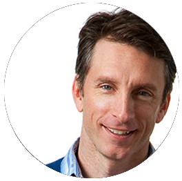 A smiling man with short brown hair, wearing a blue shirt, against a white background.