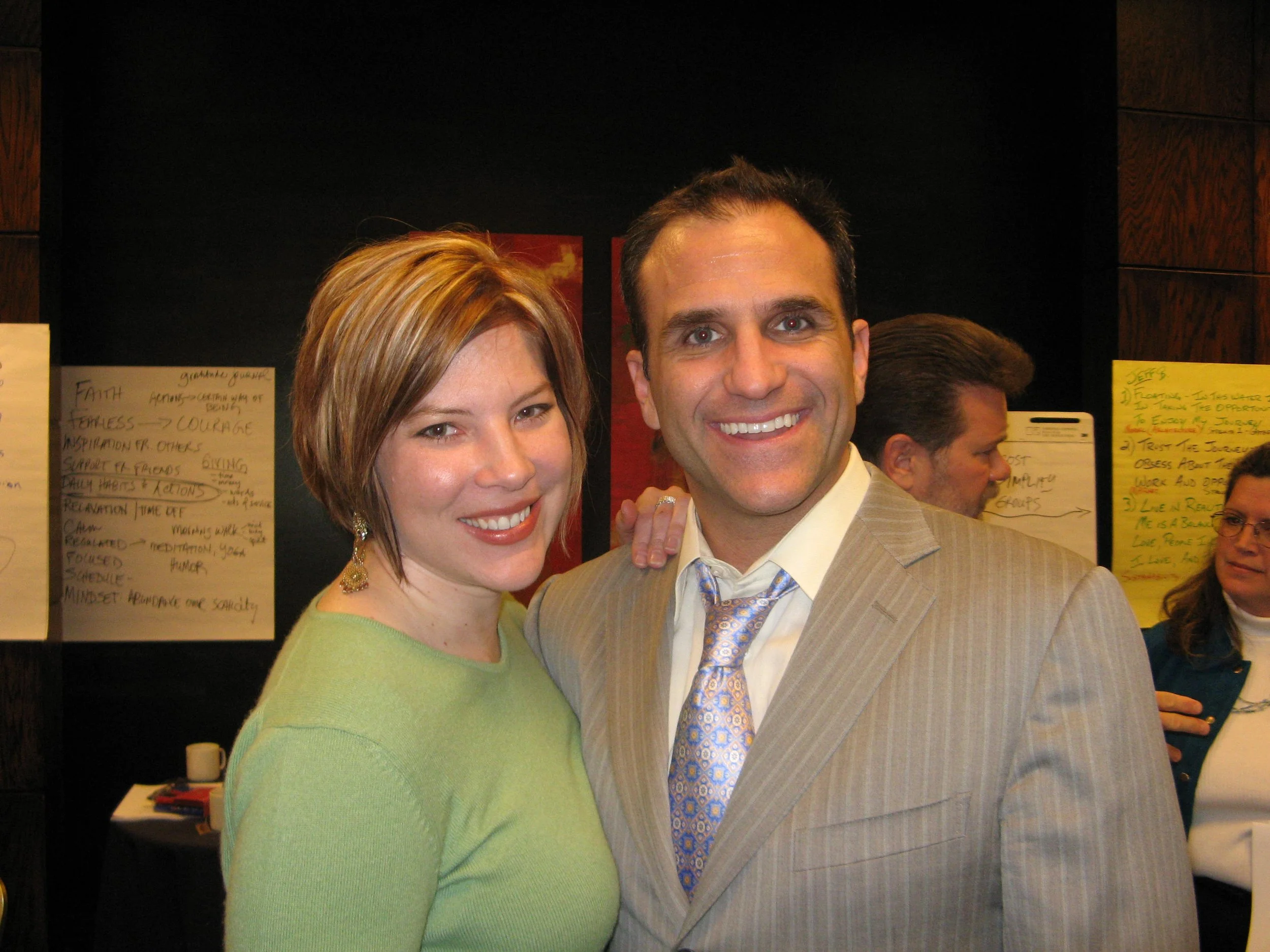 A smiling woman and man in business attire posing together at an indoor event.