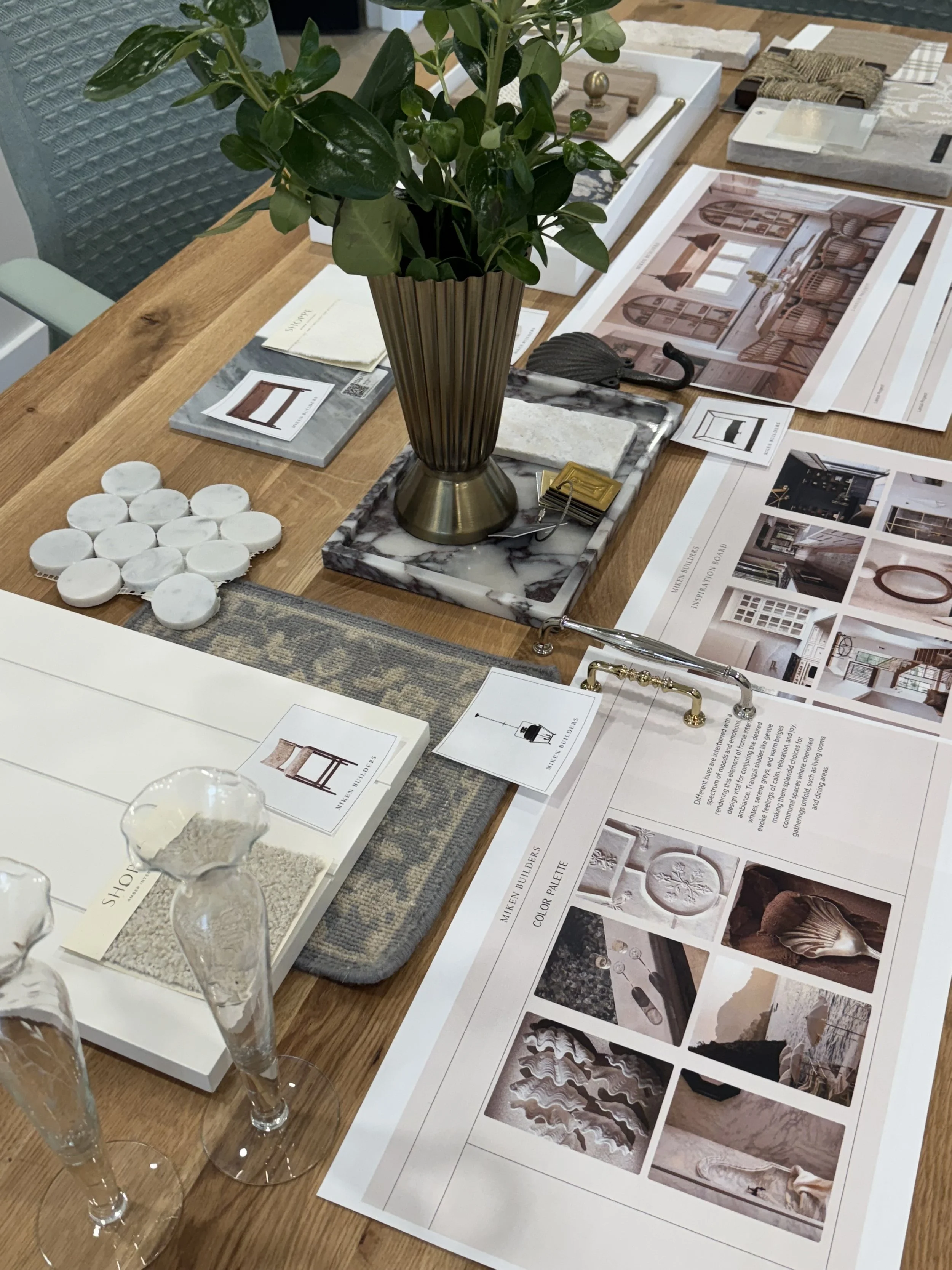 Office or design studio table with interior decoration samples, fabric swatches, architectural plans, and a green potted plant.
