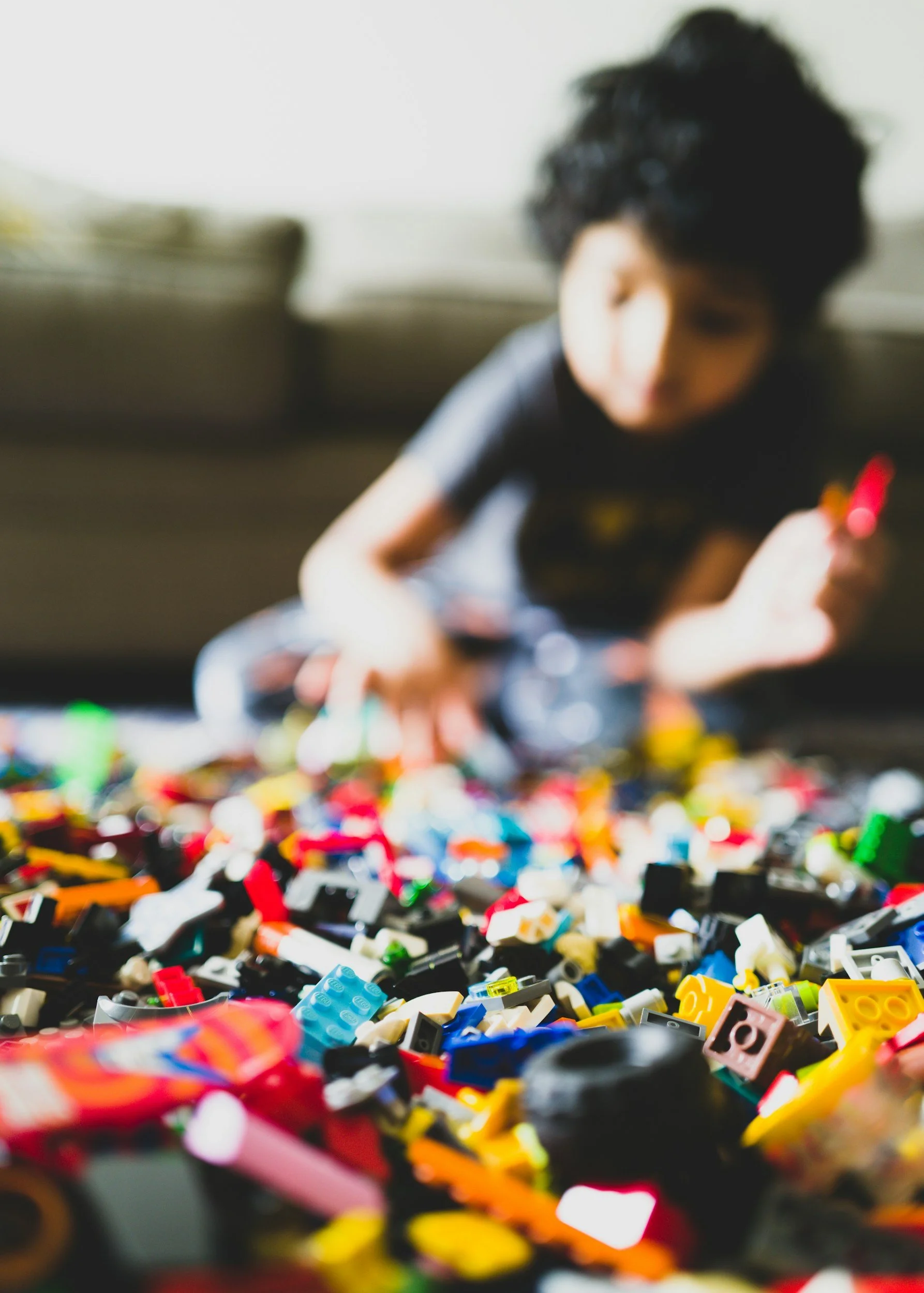 Blurred image of child with dark curly hair playing with Lego spread out in front