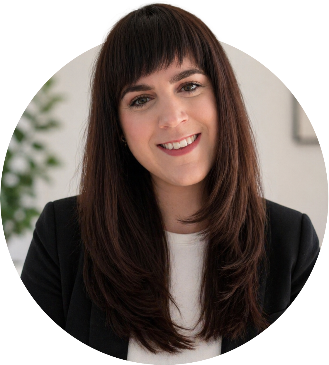 A woman with long brown hair and a friendly smile, wearing a black blazer and white shirt, in an office setting.