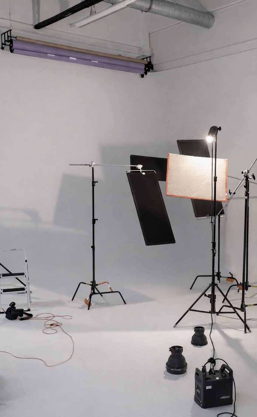 Photography studio with lighting equipment, softboxes, and backdrop stands on a white seamless backdrop.