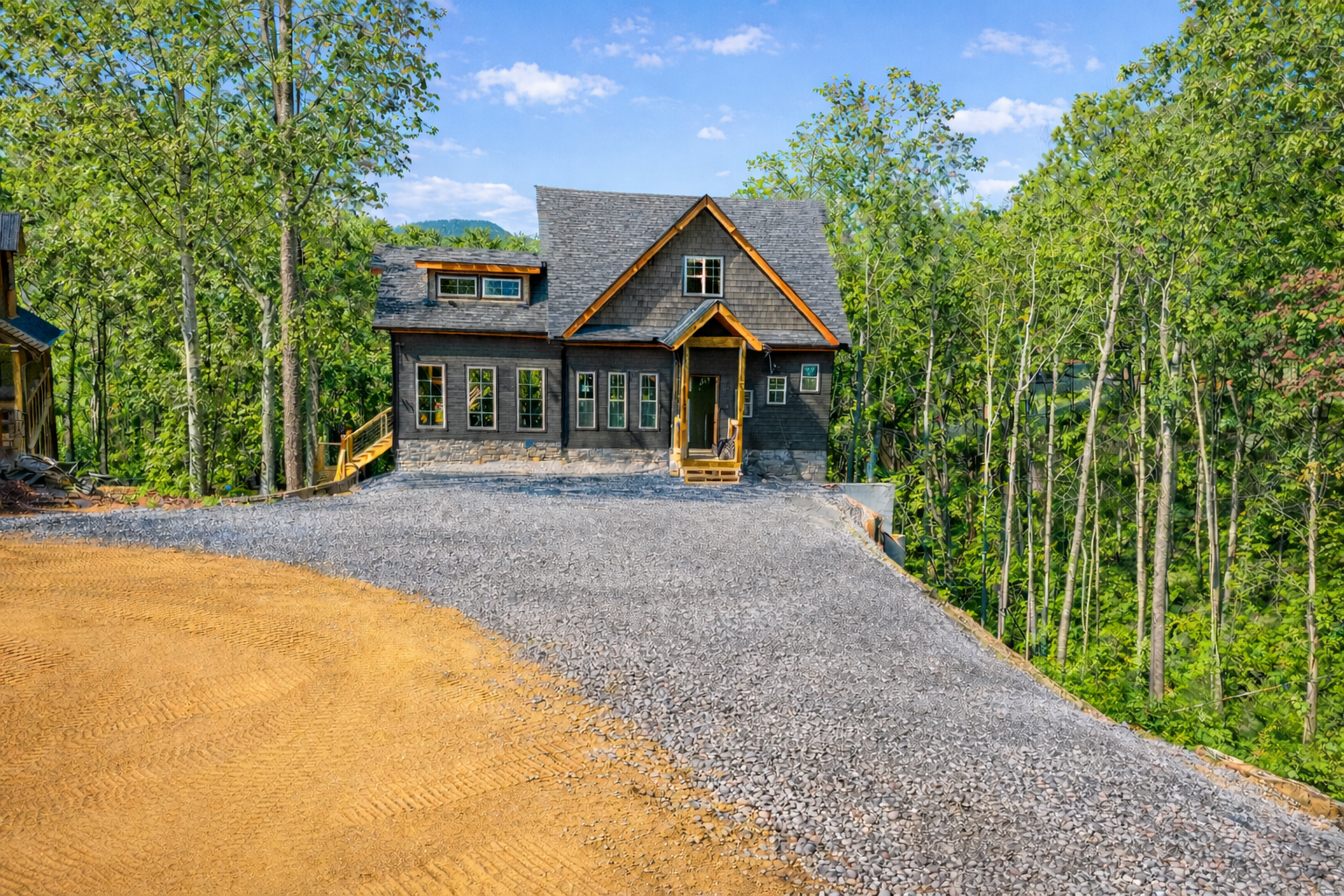 Home construction site prep in wooded East Tennessee lot with gravel driveway and grading