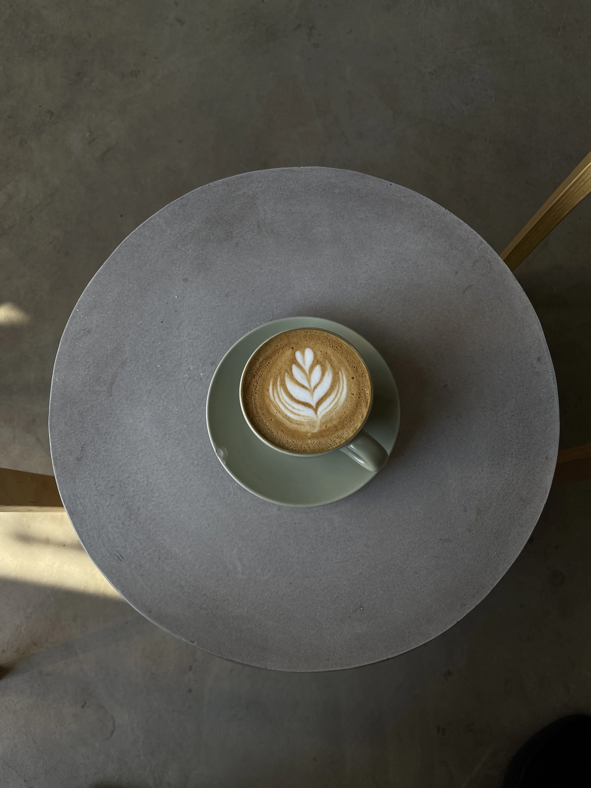 A cup of coffee with latte art in a light green cup and saucer on a gray round table.