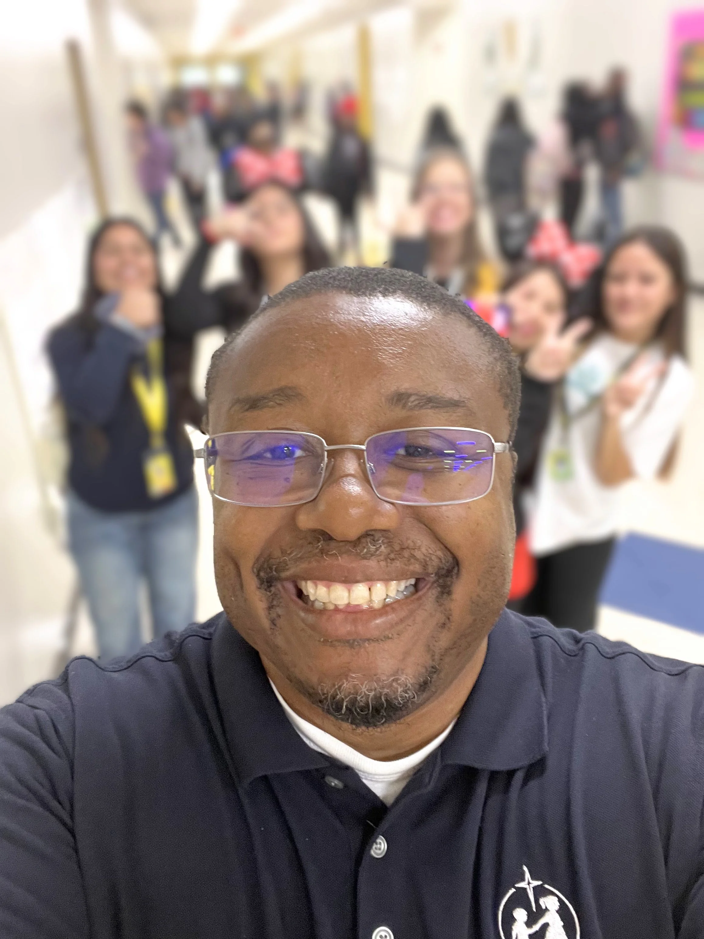 Dr. Mackins with students blurred in the background, making peace signs and showing their love and support for their teacher and mentor.