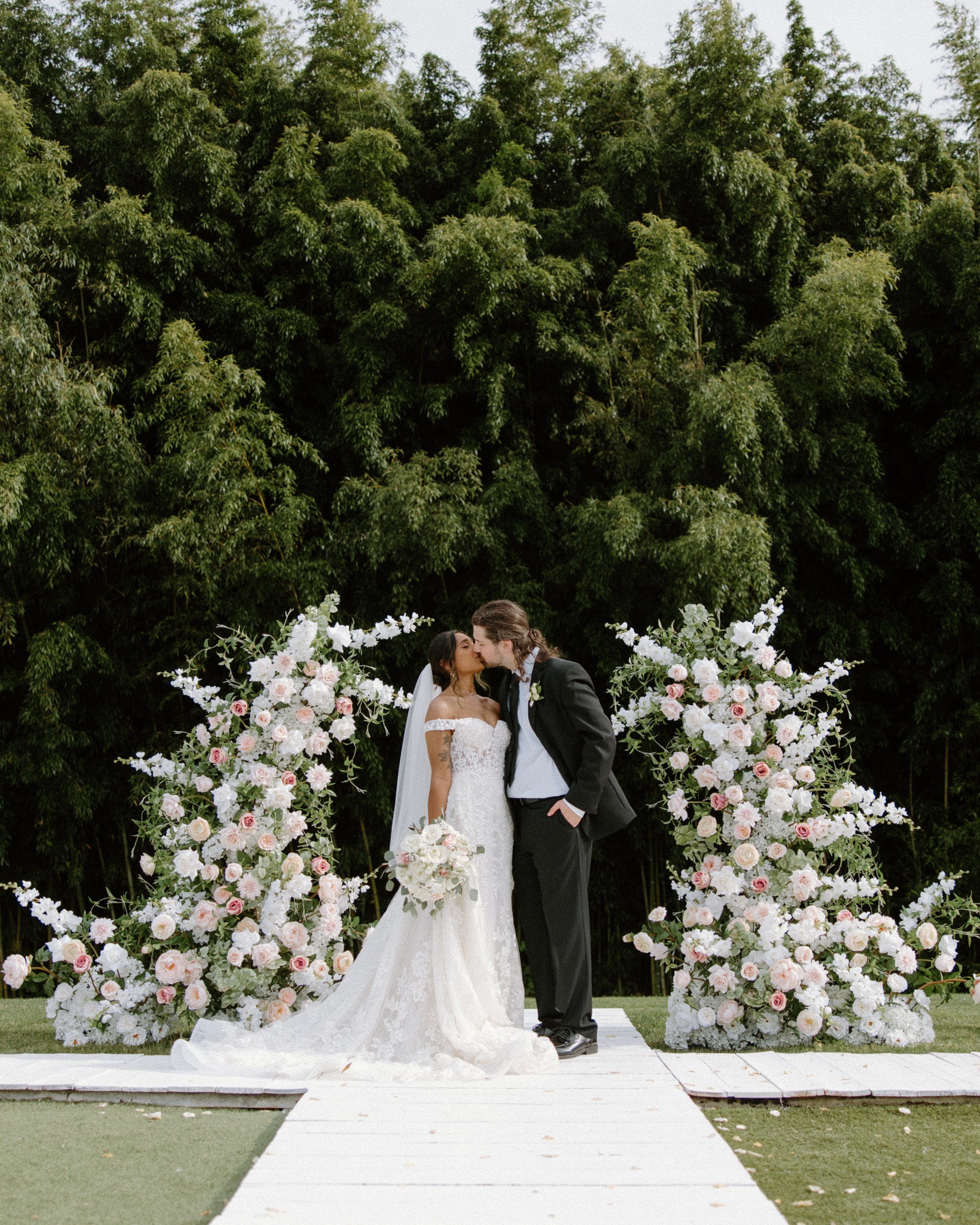 Bride and Groom kissing under floral arch and forest at Camelot Meadows wedding venue