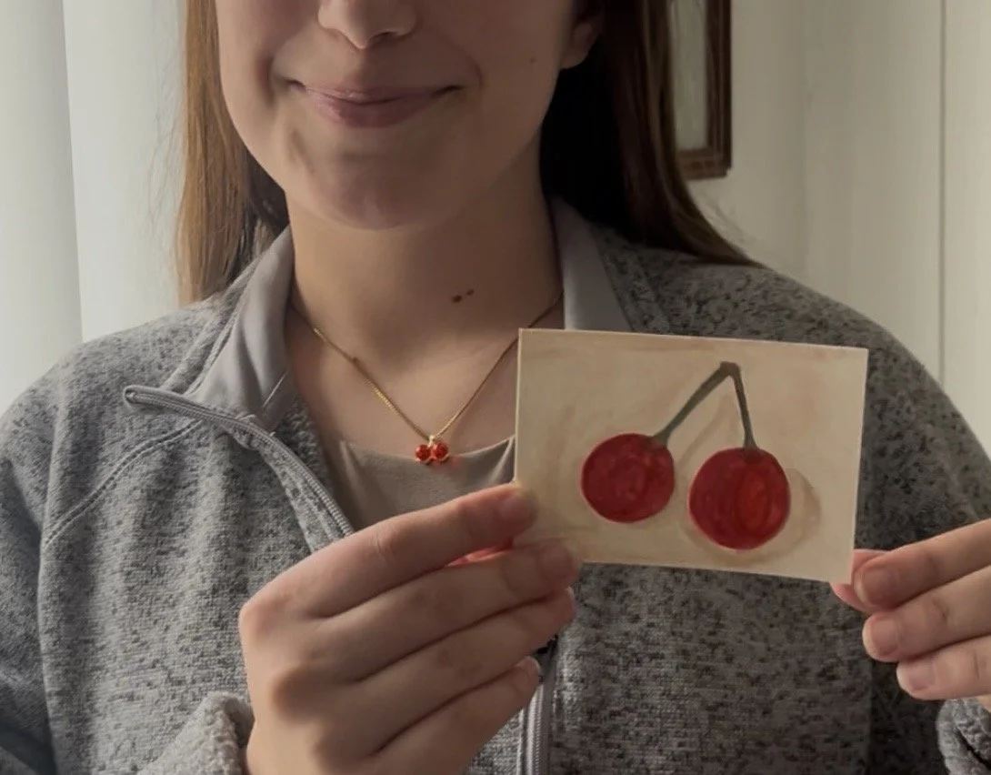 Alyssa is holding a painting of two cherries inspired by her necklace.