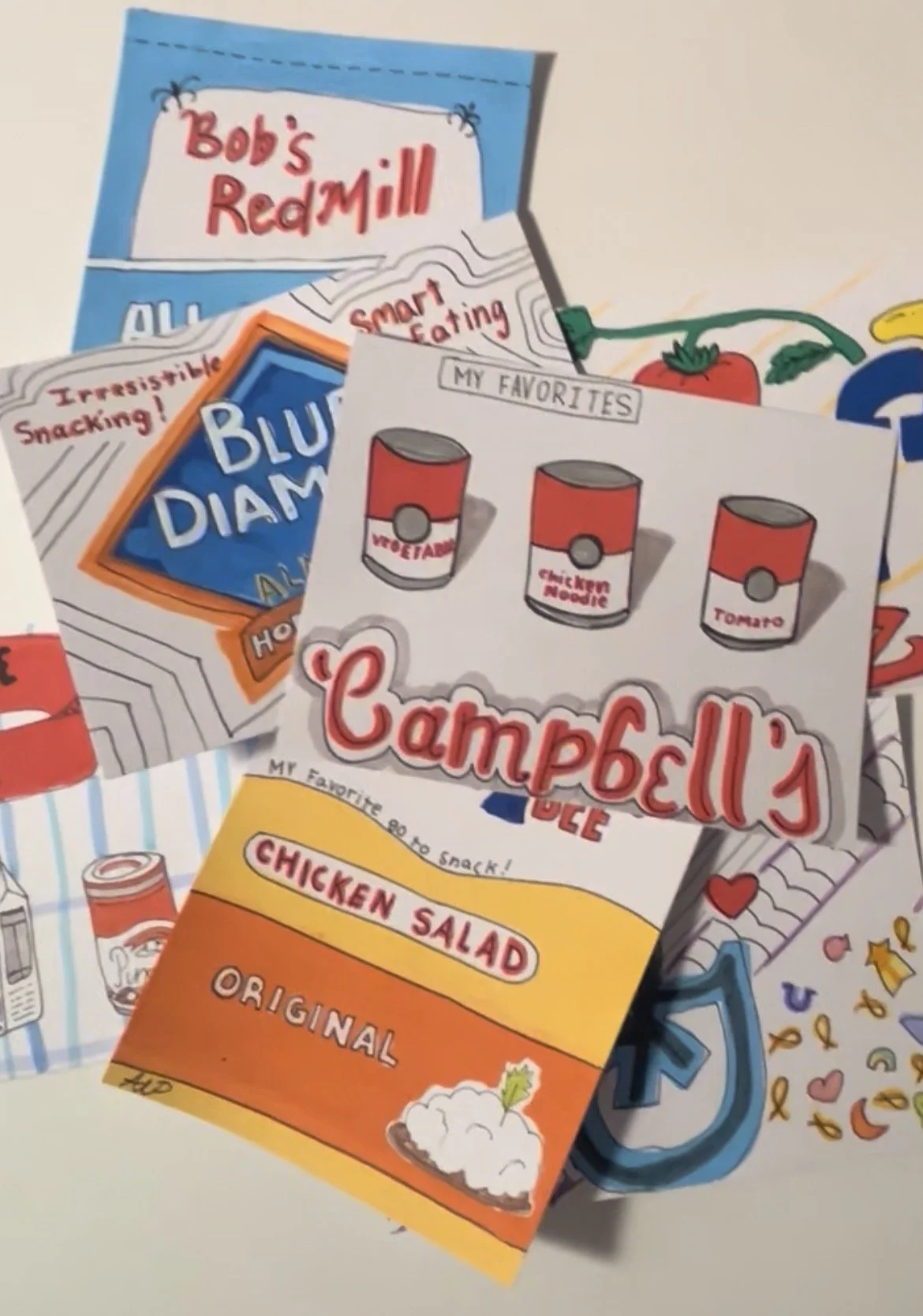 Close-up of a colorful painted paper featuring Campbell's soup cans, a chicken salad sandwich label, and various lunch-related illustrations and text.