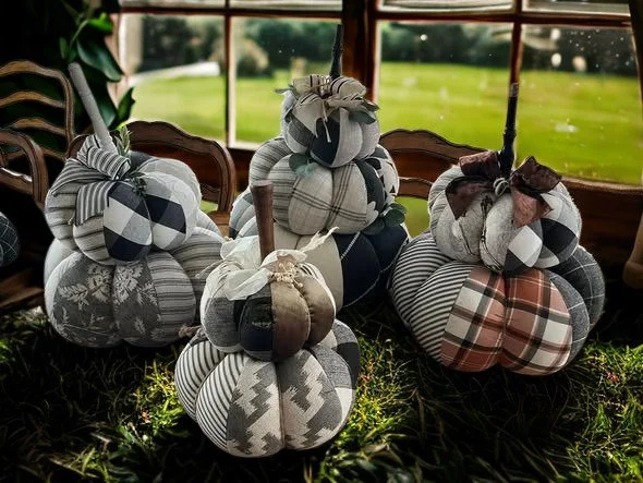 Decorative fabric scarecrows made of patchwork cloth with tied fabric hats, arranged indoors in front of a window with a grassy outdoor view.