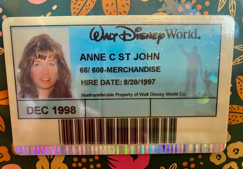Walt Disney World employee ID badge for Anne C St John, MC-600 merchandise, hired on August 20, 1997, with a photo of a woman and a barcode, dated December 1998.