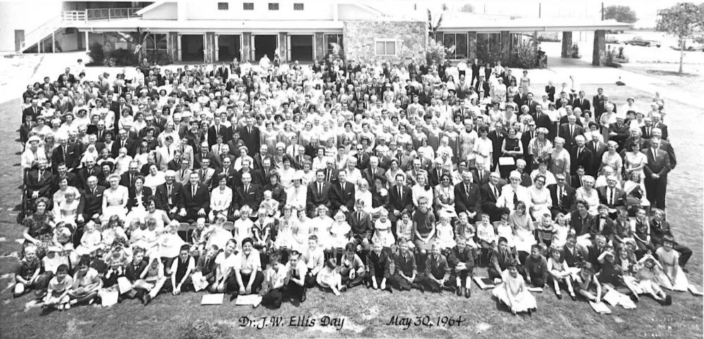 A large black and white group photograph taken outdoors in front of a building, featuring many adults and children seated and standing, with a caption at the bottom reading 'Dr. J.W. Ellis Day, May 30, 1964'.
