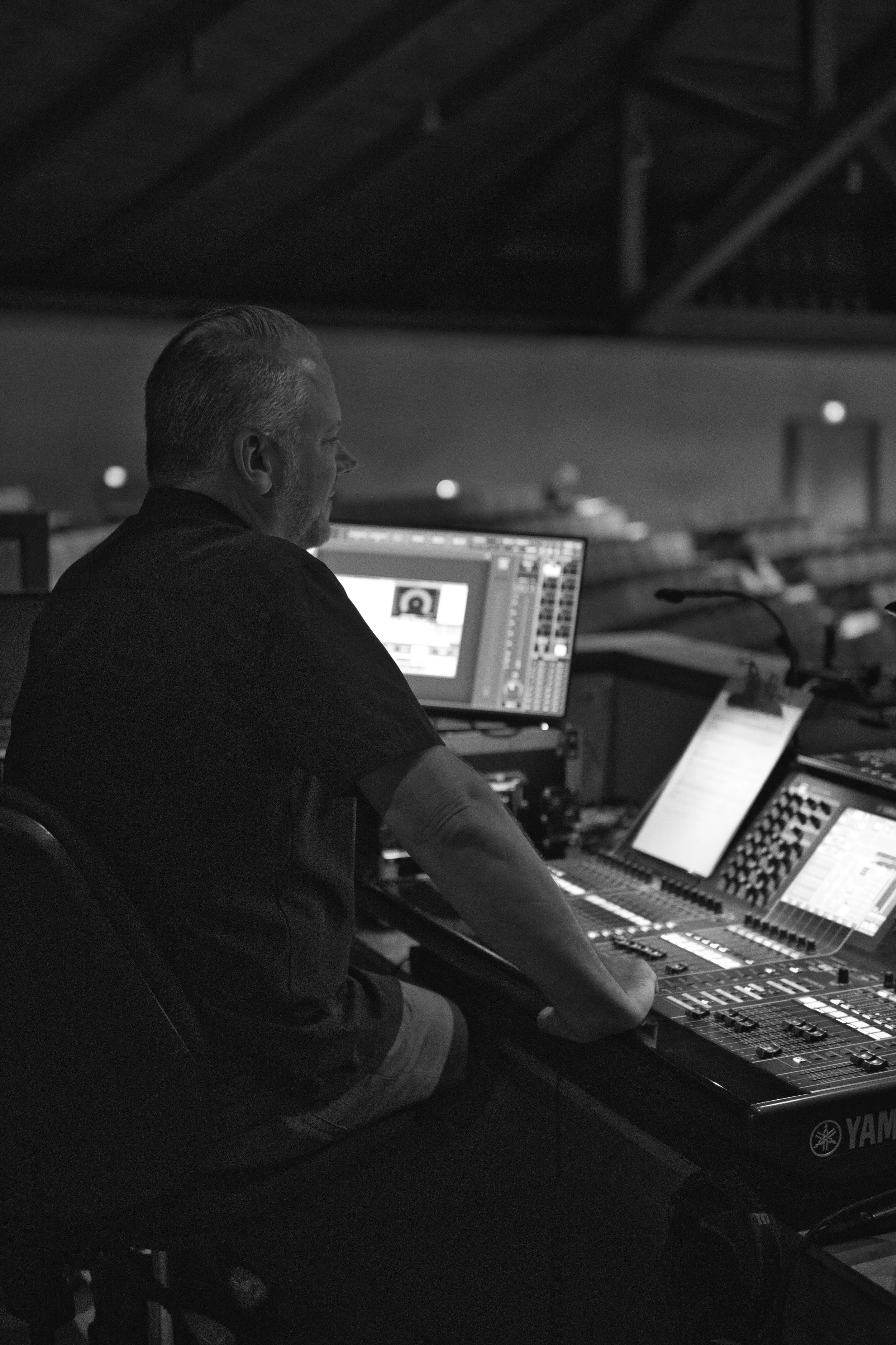 A man with gray hair working on audio mixing equipment in a dimly lit room.