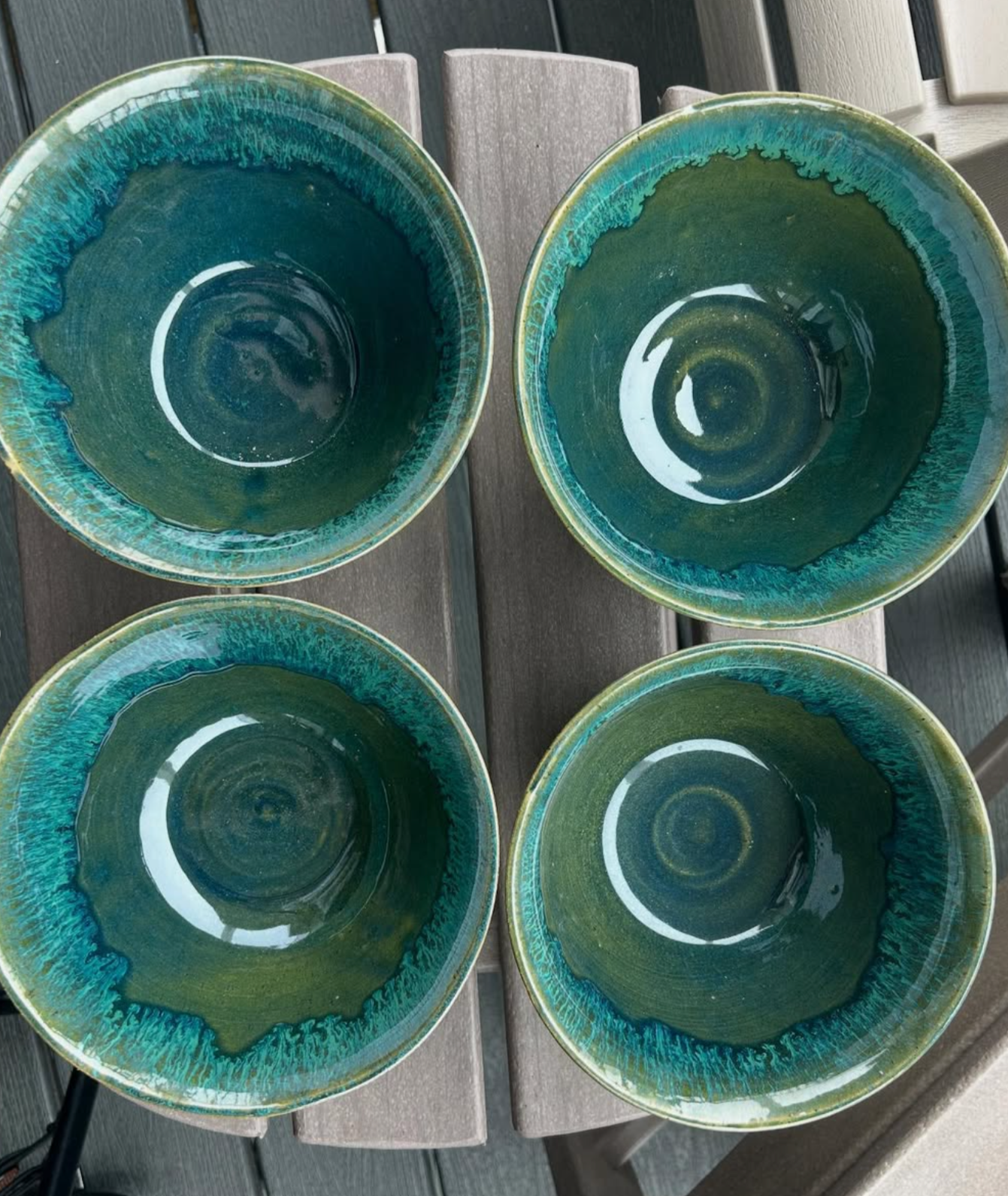 Four ceramic bowls with greenish-blue glaze, placed on a grey wooden surface.