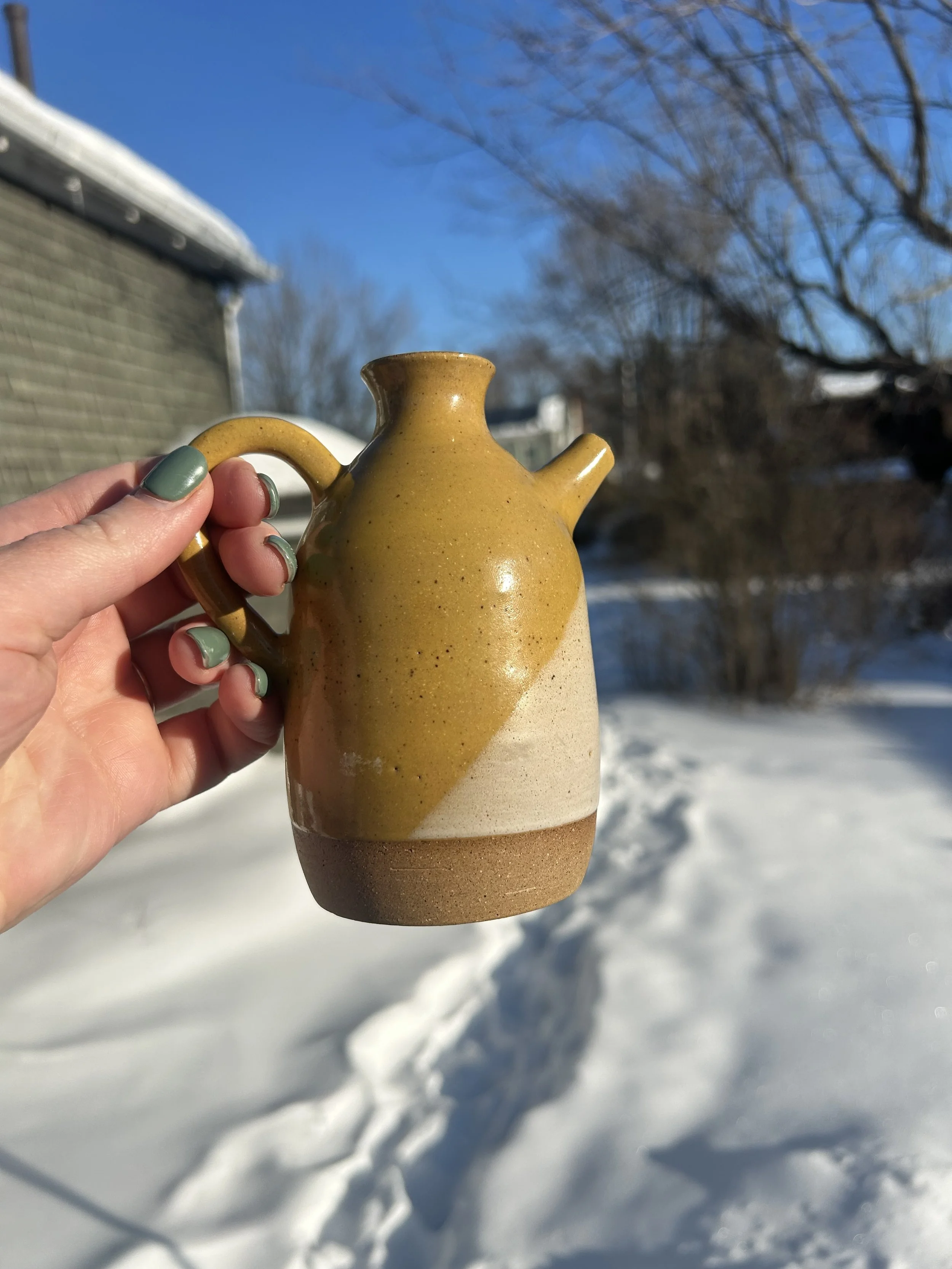 A person holding a ceramic teapot outdoors in winter with snow on the ground and bare trees in the background.