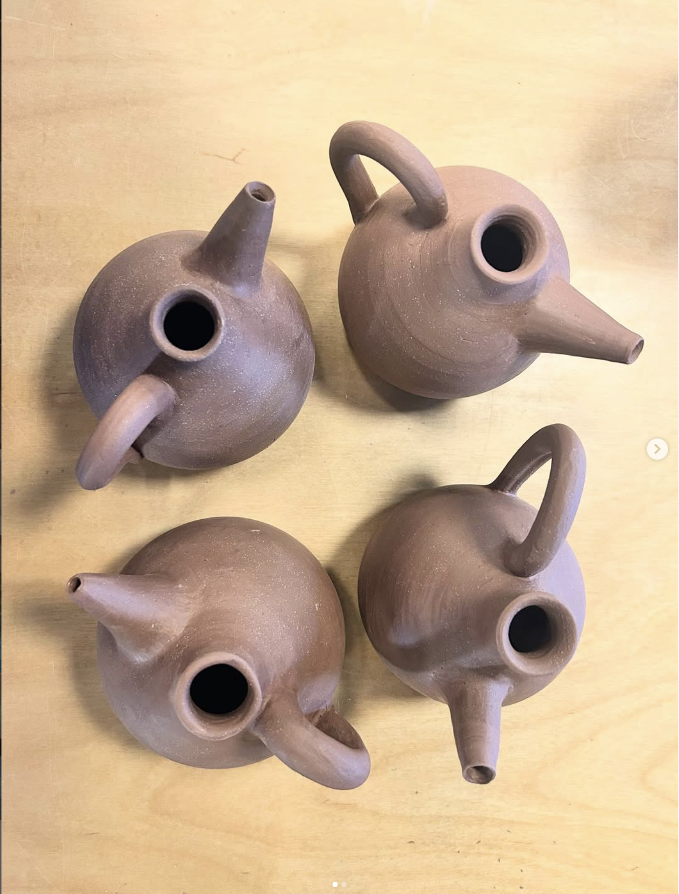 Several unfinished ceramic teapots with spouts, handles, and open tops on a wooden table.
