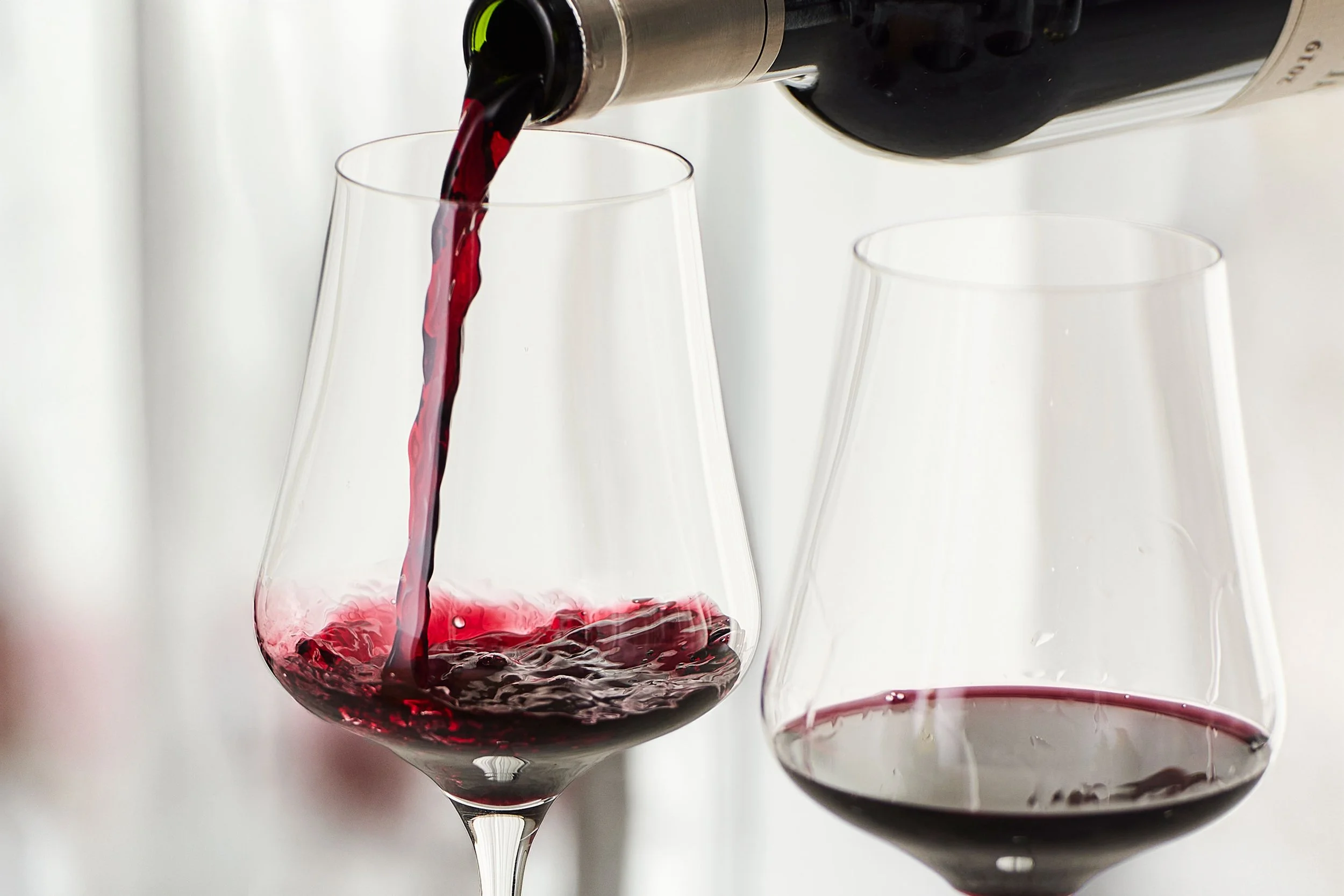 Red wine being poured into a wine glass, with additional glasses in the background.