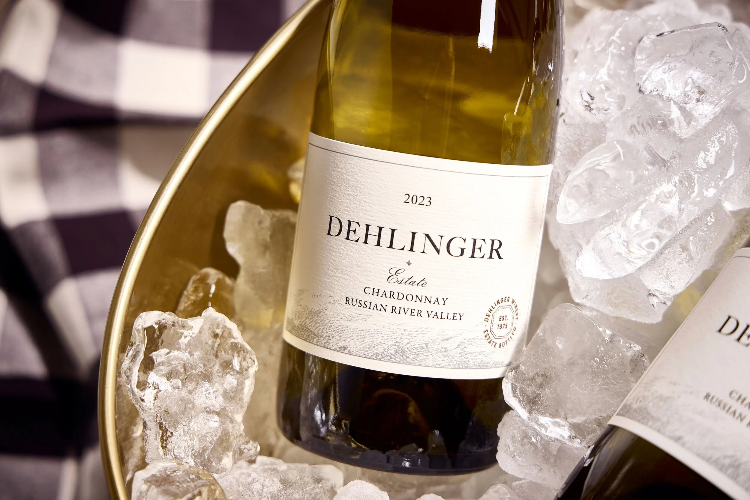 A bottle of Dehlinger Estate Chardonnay wine from the Russian River Valley in 2023, placed on ice in a circular container, with ice cubes surrounding it.