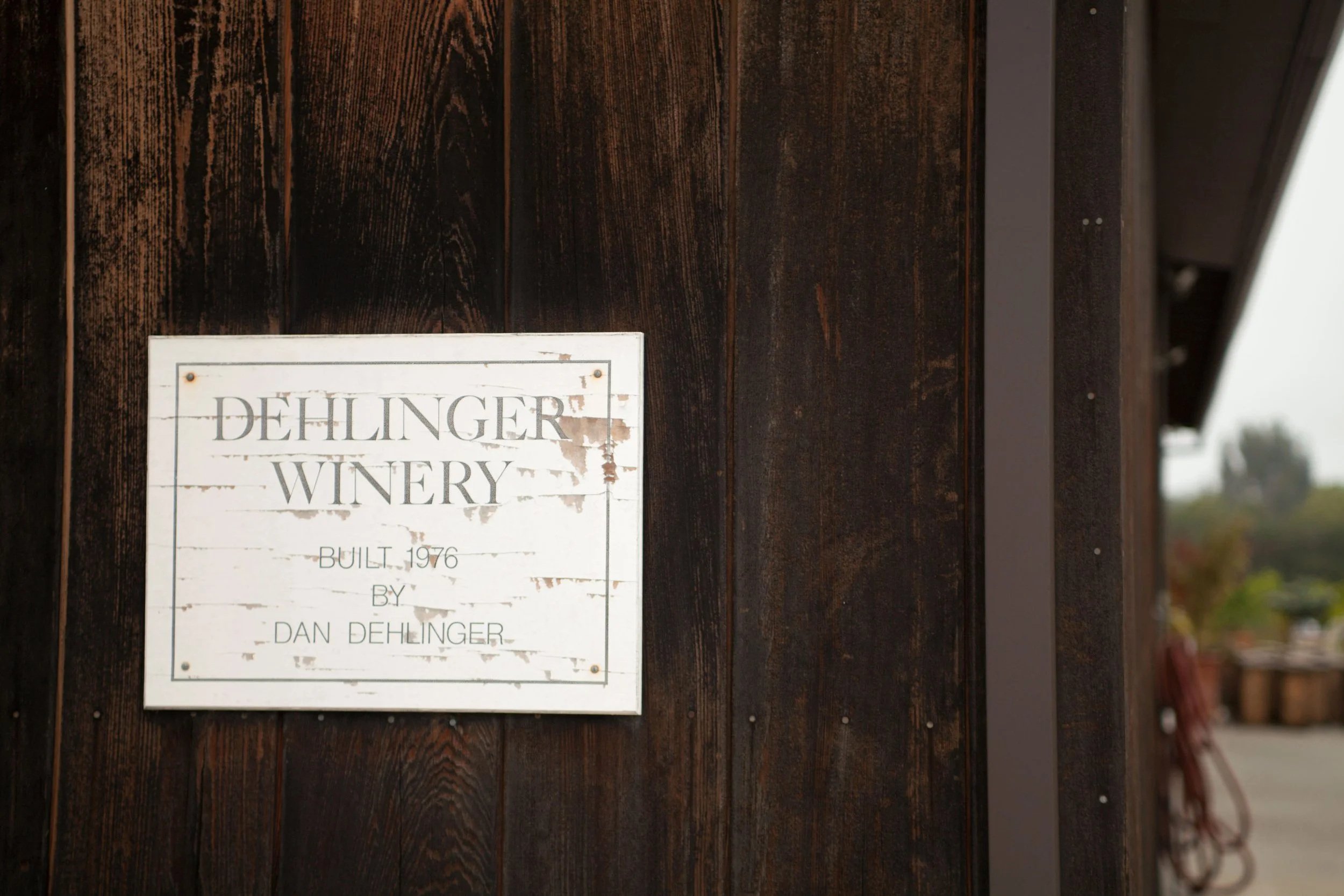 Wooden sign on a dark wooden wall that reads "Dehlinger Winery Built 1976 by Dan Dehlinger."