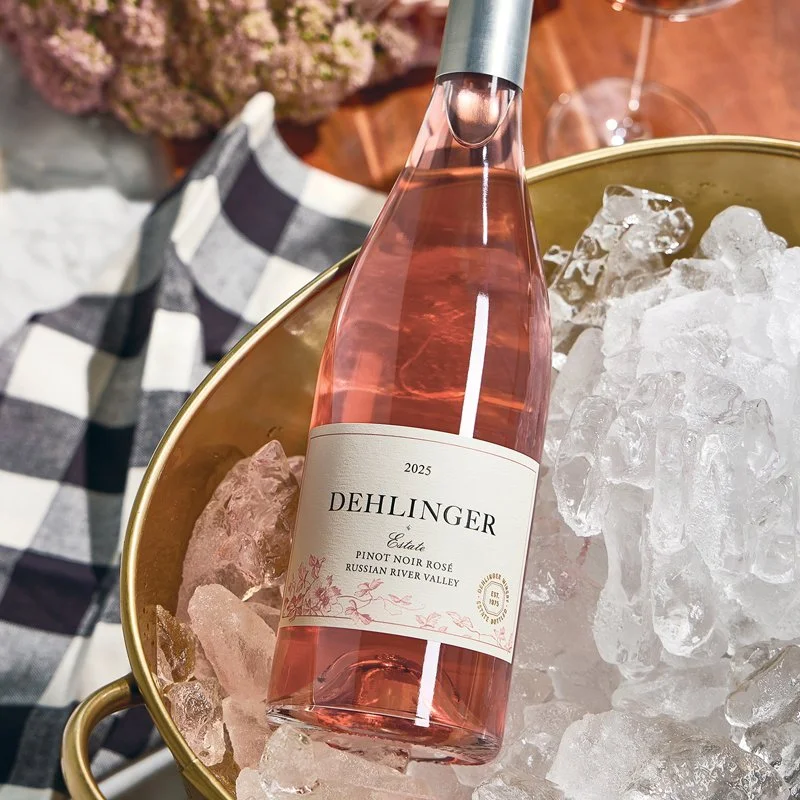 A bottle of Dehlinger Estate Pinot Noir Rosé 2025 in a gold ice bucket filled with ice, with a checkered black and white cloth in the background.