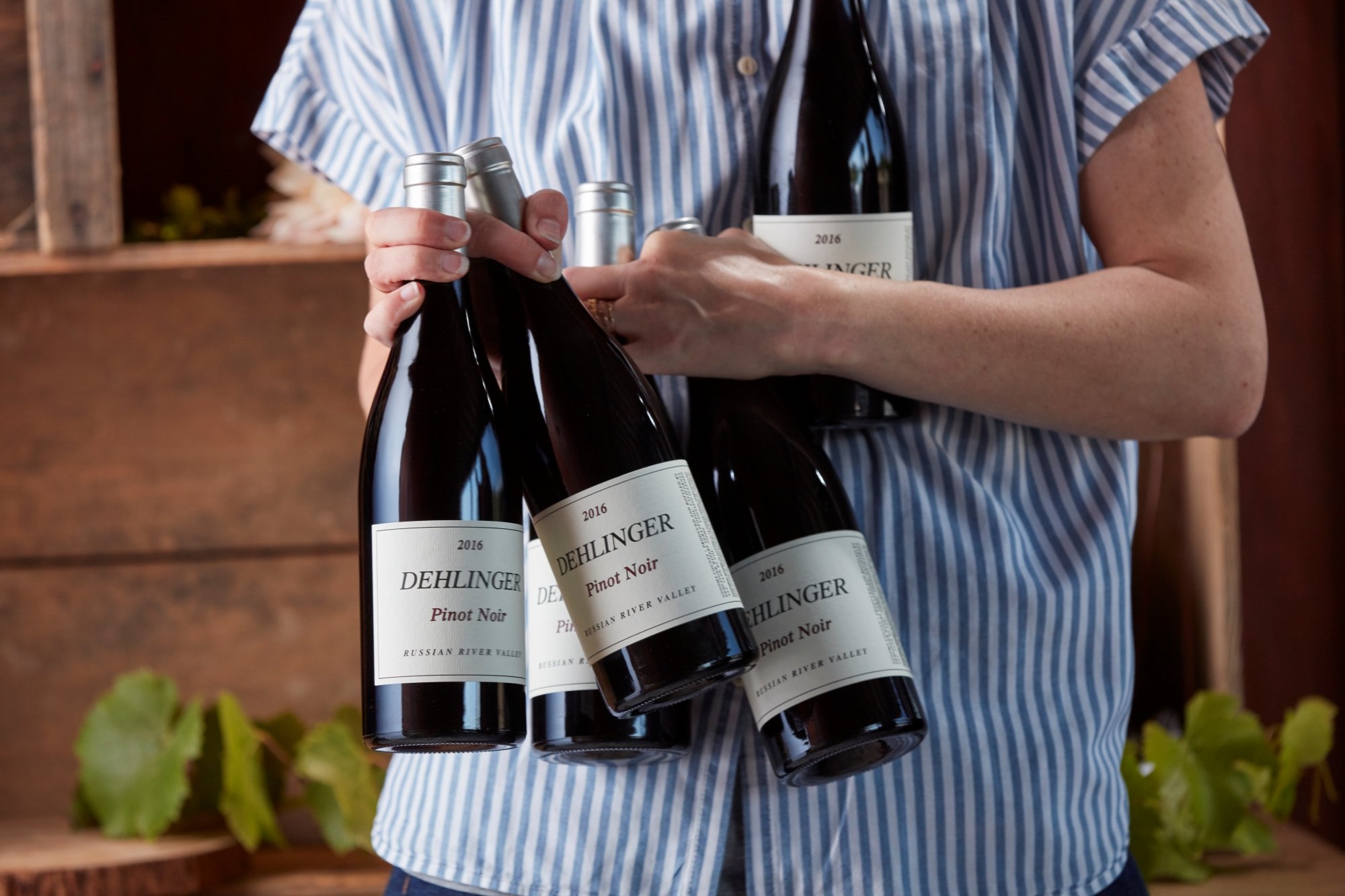 Person holding several bottles of Dehlinger Pinot Noir wine in a casual setting.