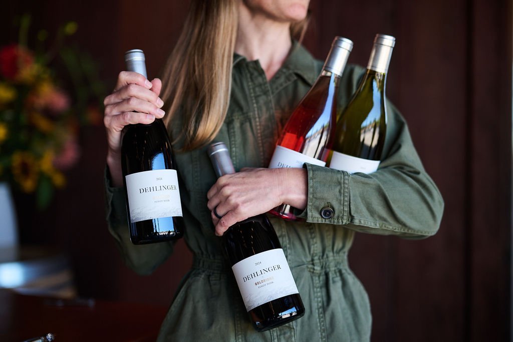 A woman triumphantly holds four bottles of Dehlinger wine