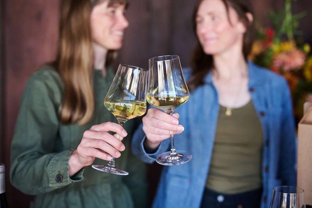 Two glasses clinking festivally with the faces of two smiling women in the background
