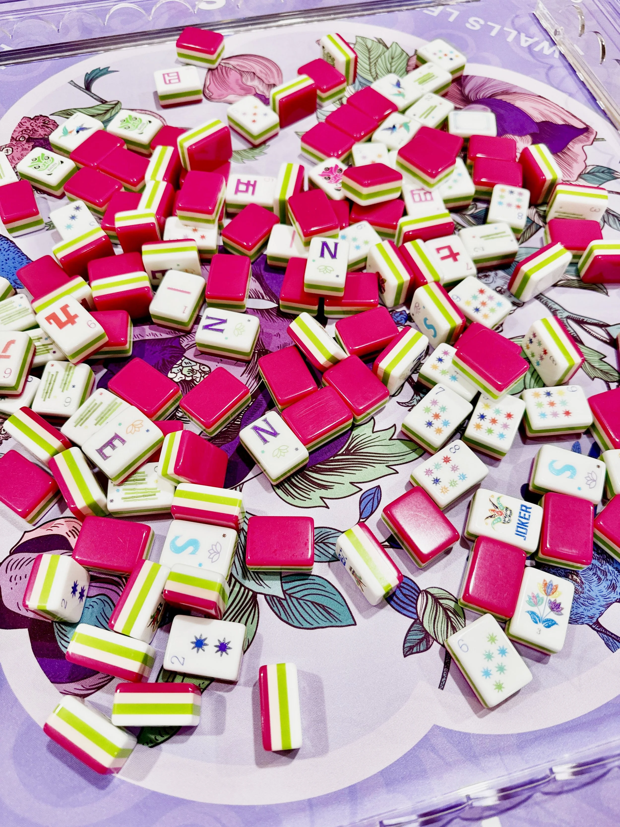 A collection of dominoes scattered on a decorative surface with floral and leaf patterns, some showing colorful designs and numbers.