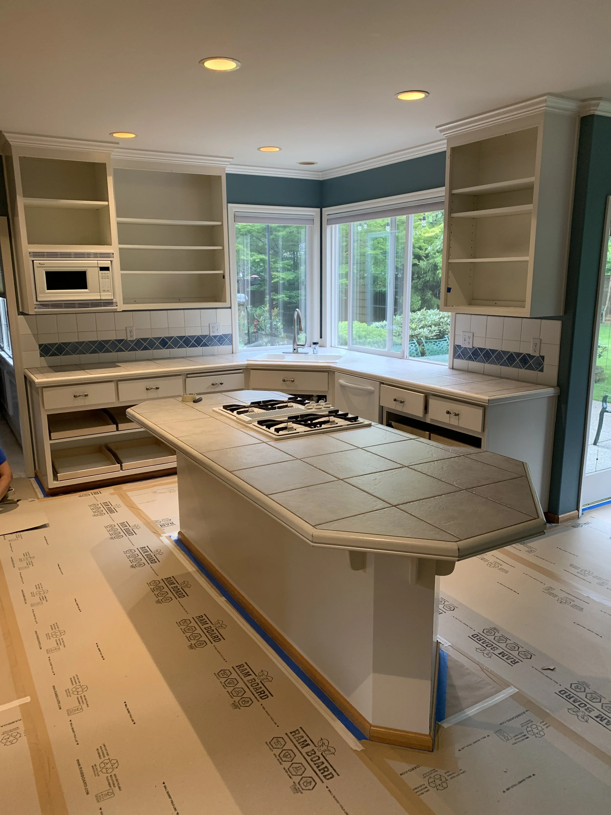 Kitchen with beige tile countertop island, white cabinetry, open shelves.