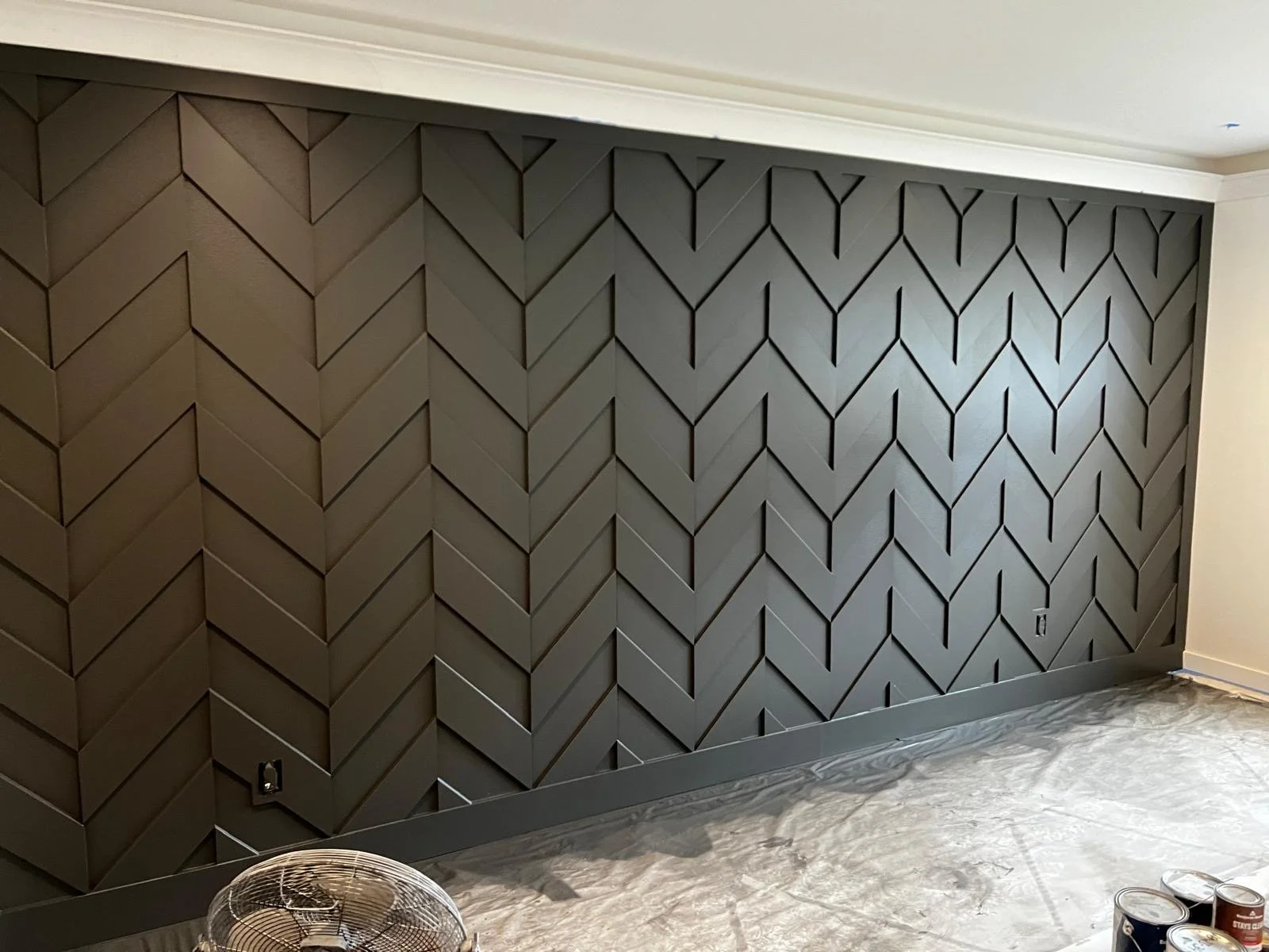A room with a geometric-patterned dark gray accent wall and a plastic sheet covering the floor.