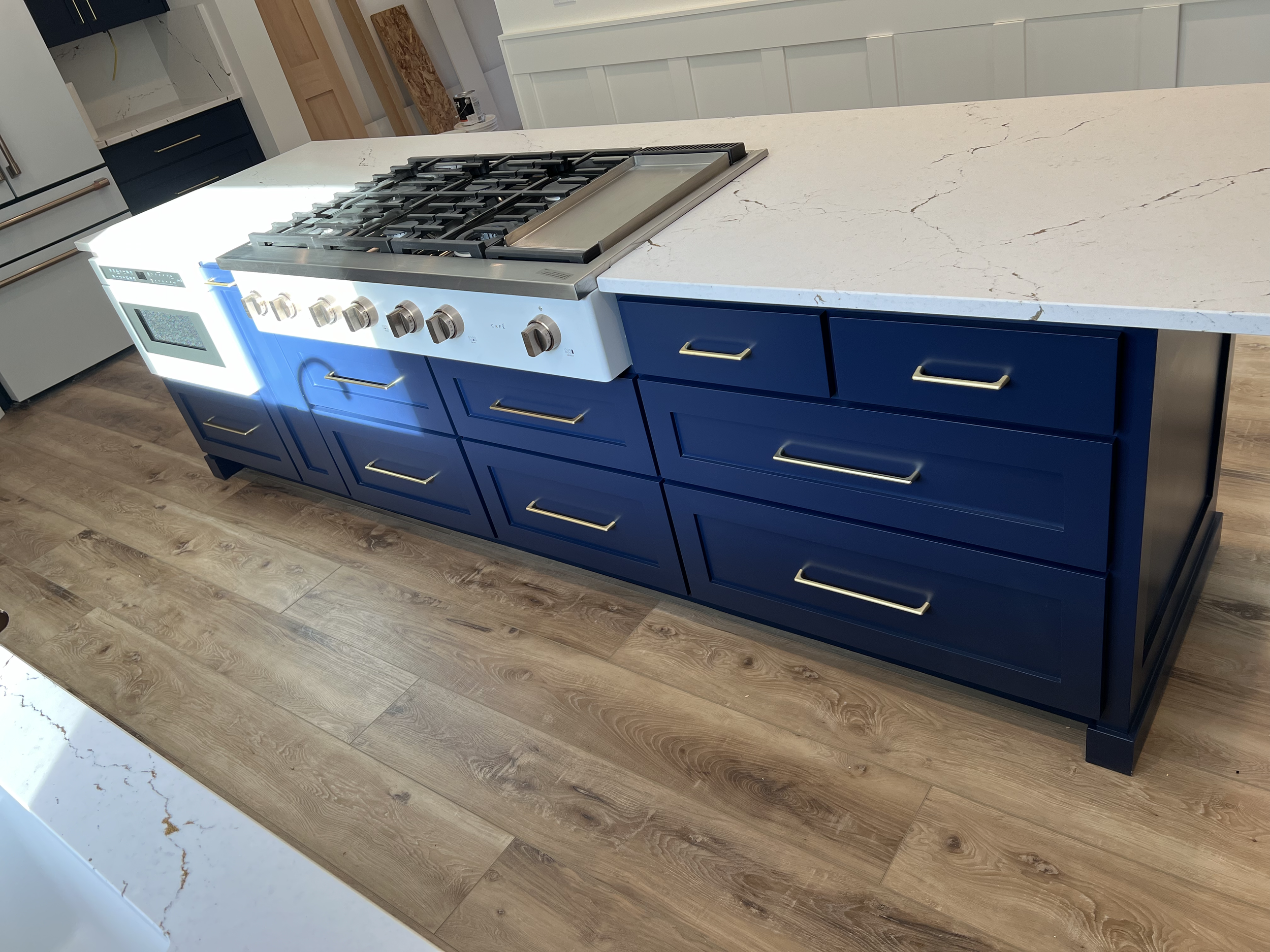 A modern kitchen island with dark blue cabinets, gold handles, and a white marble countertop. It features a stainless steel gas cooktop with multiple burners.