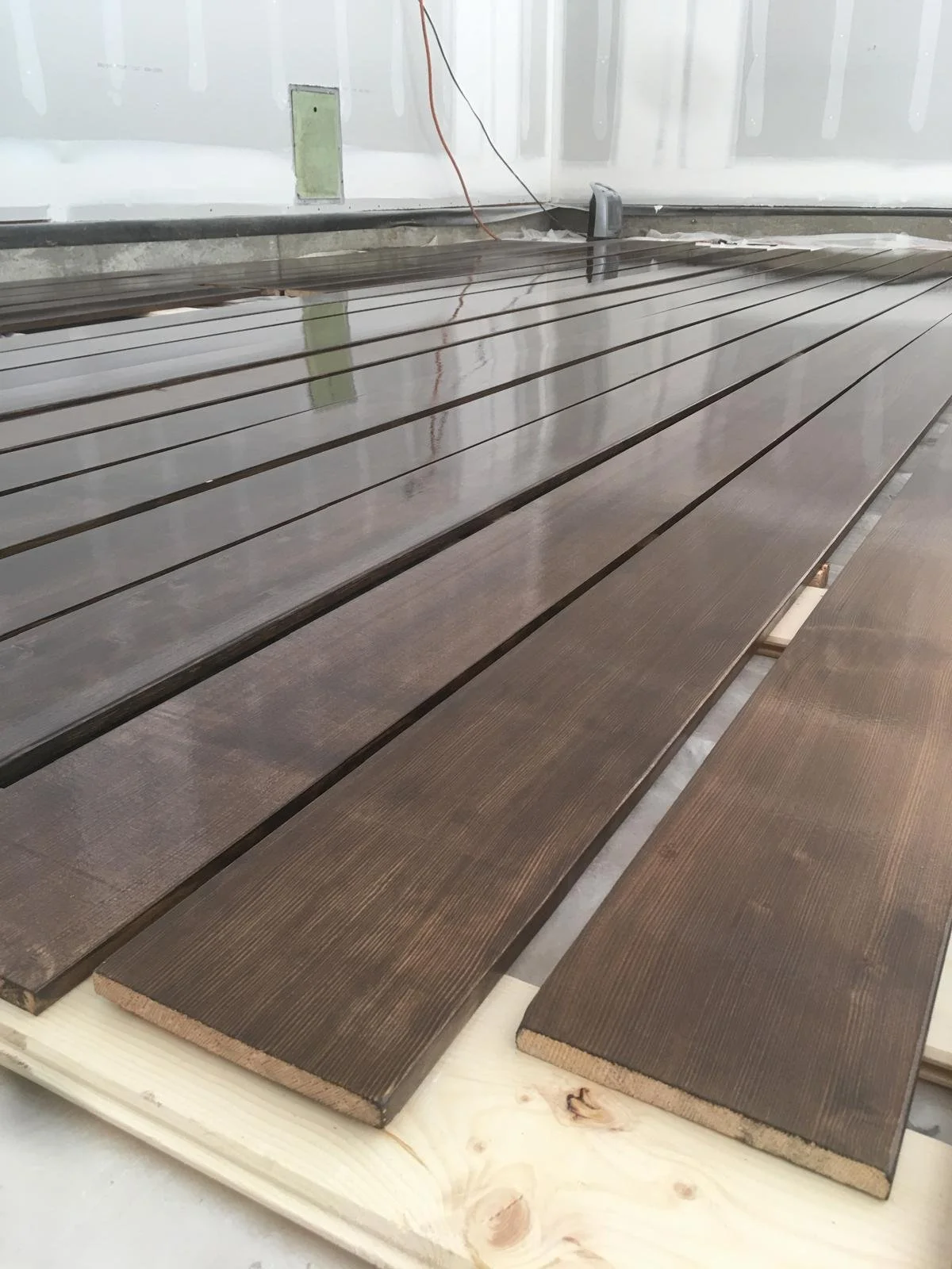 Several wooden planks laid out on a construction site with unfinished drywall and electrical wiring visible in the background.