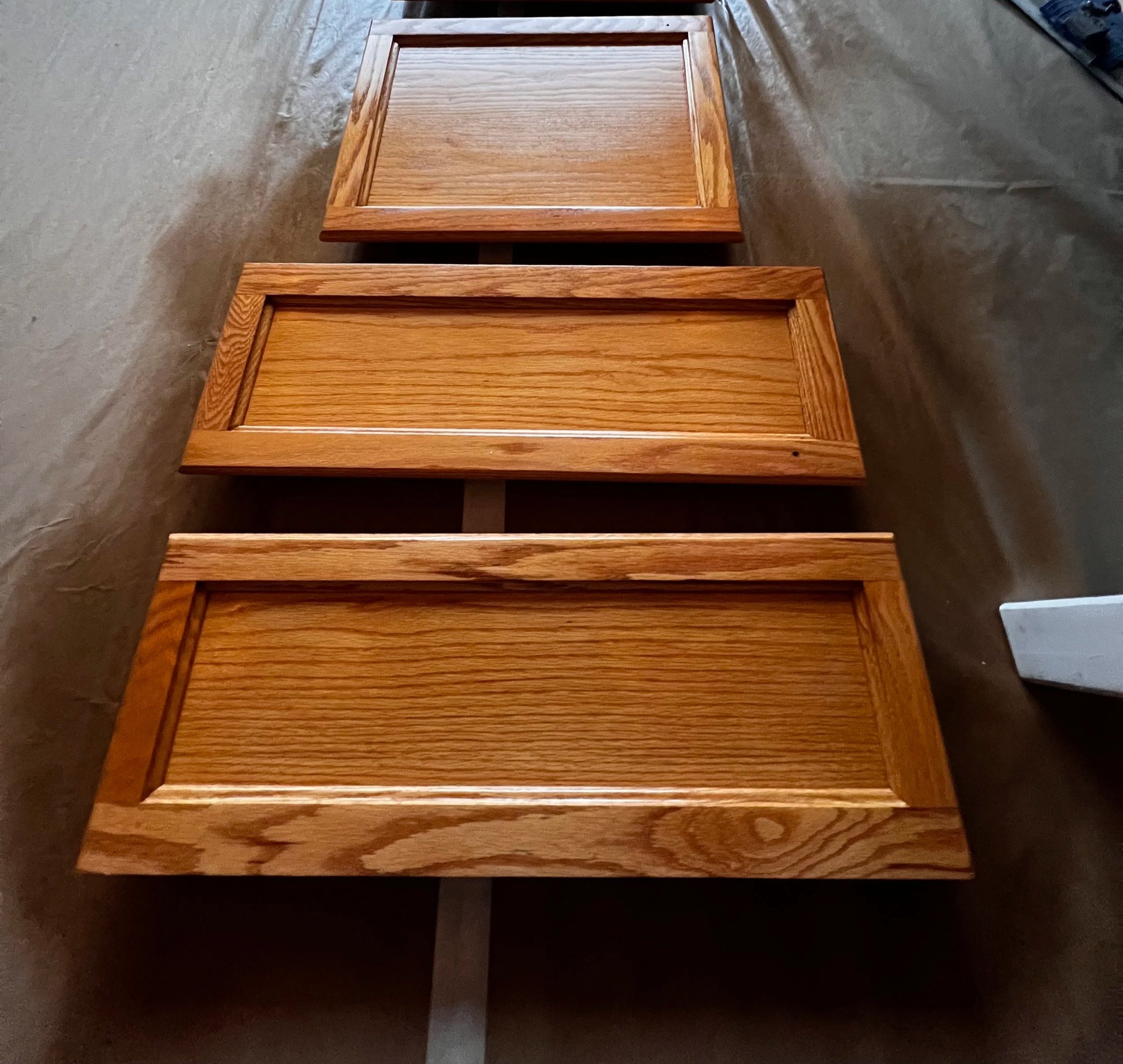 Three wooden drawer fronts laid flat on a surface, showing the front panels with a natural wood finish and beveled edges.