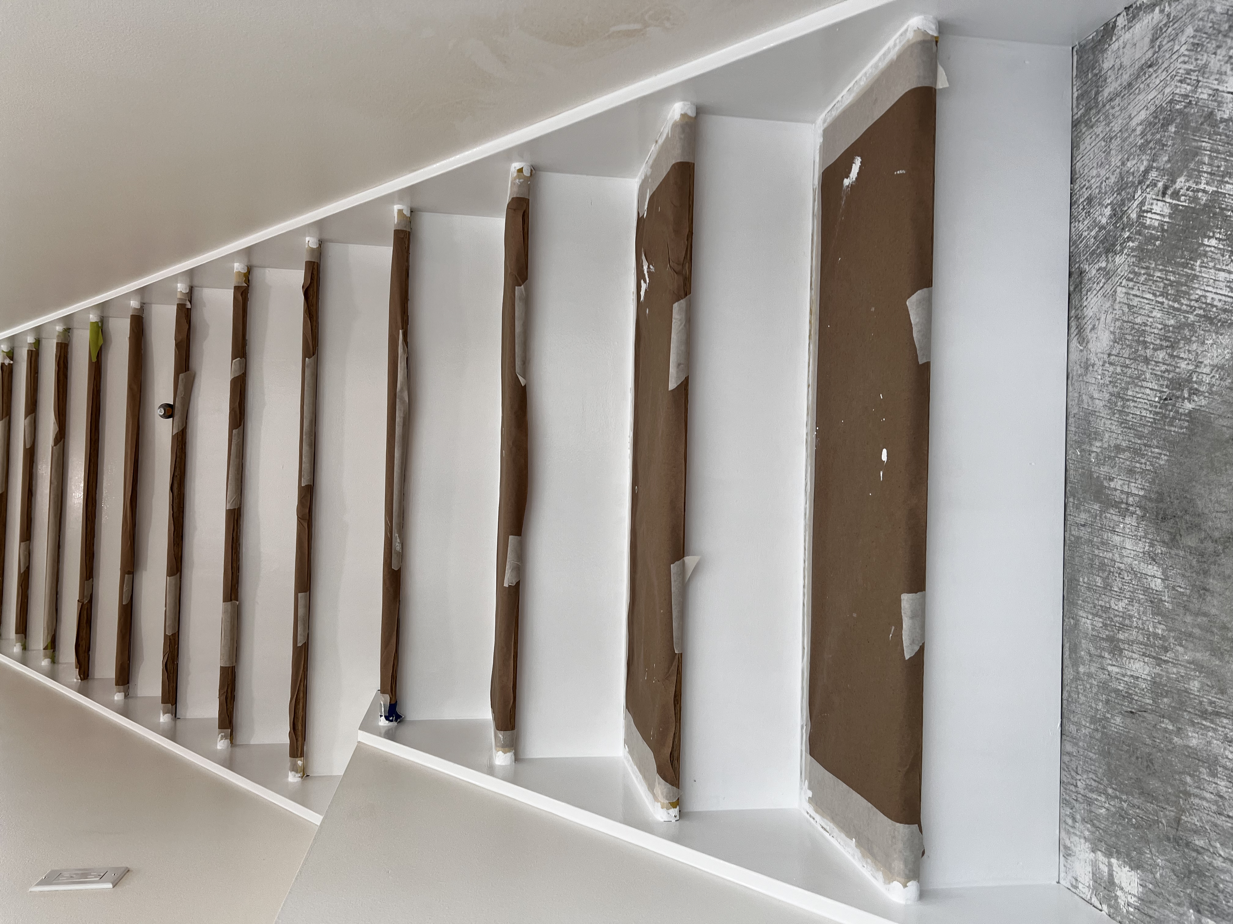 Undergoing renovation, staircase with brown paper covering the steps and white paint on the risers, next to a textured grey floor.