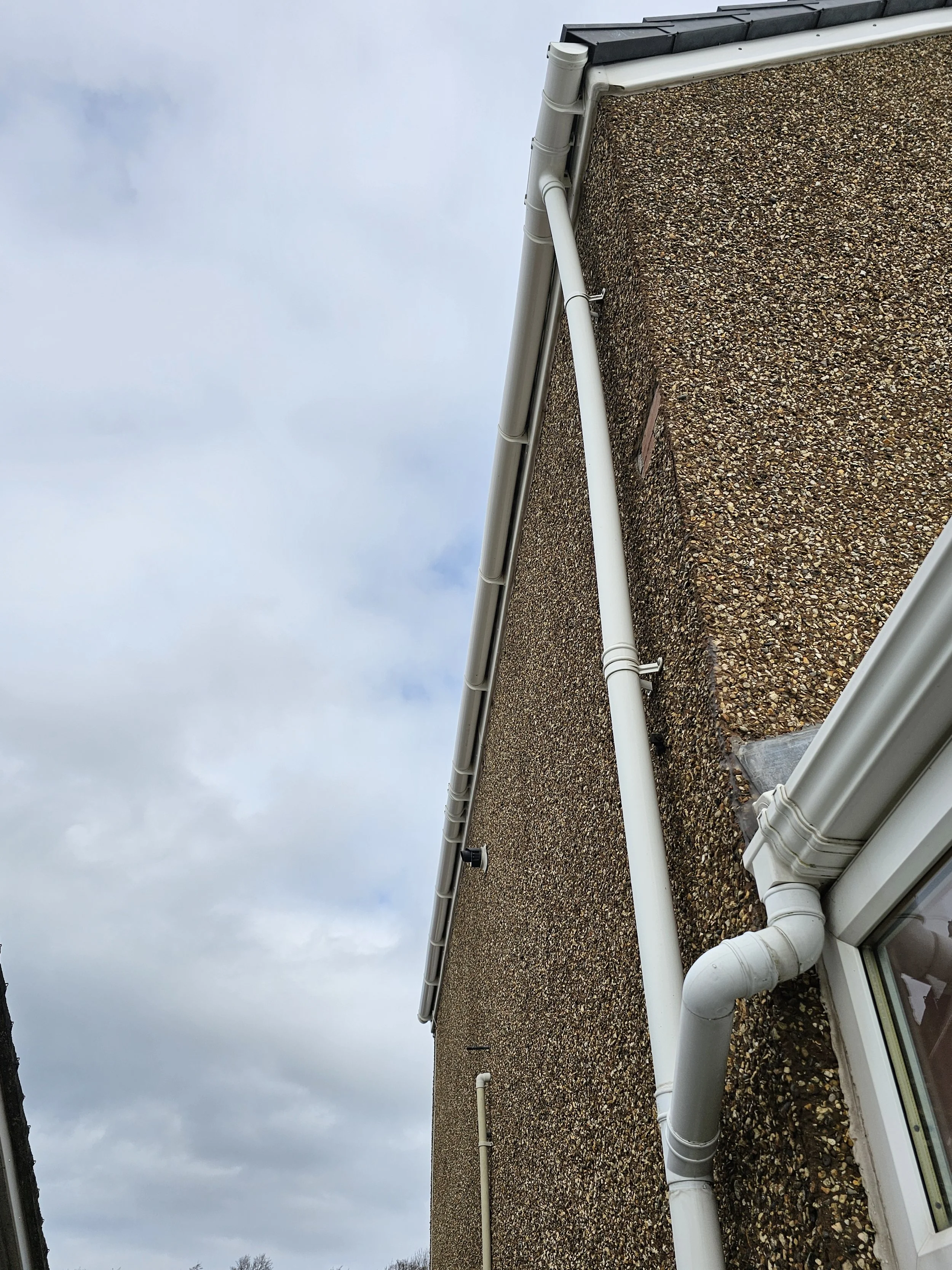 View of a rooftop with a brown gravel surface and white rain gutters and pipes, against a cloudy sky.