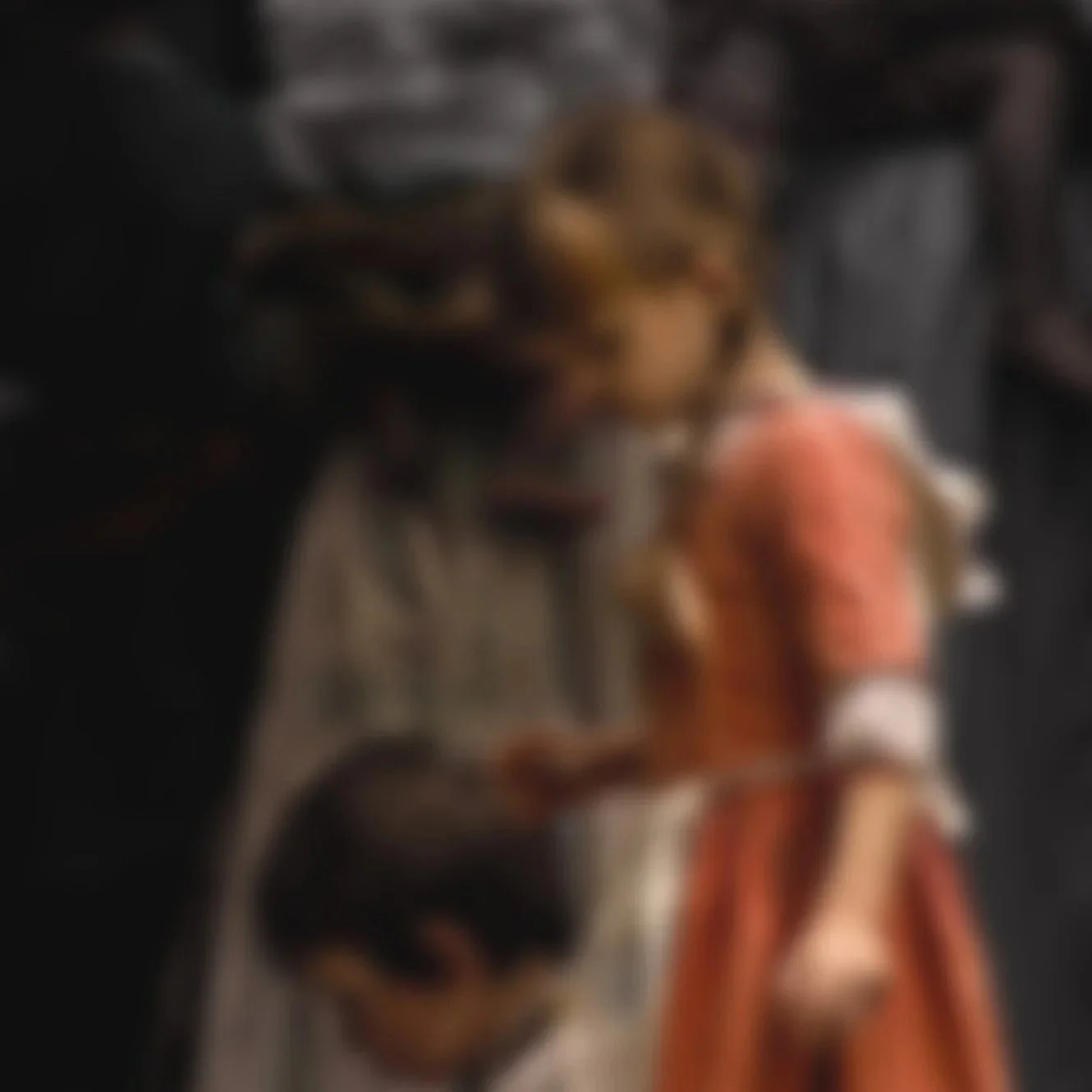 A person with curly hair wearing a beige jacket near a statue.