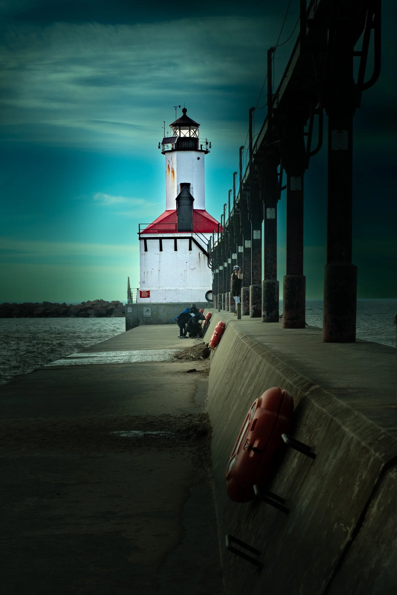 A lighthouse on a pier, with a few people near it, under a cloudy sky.