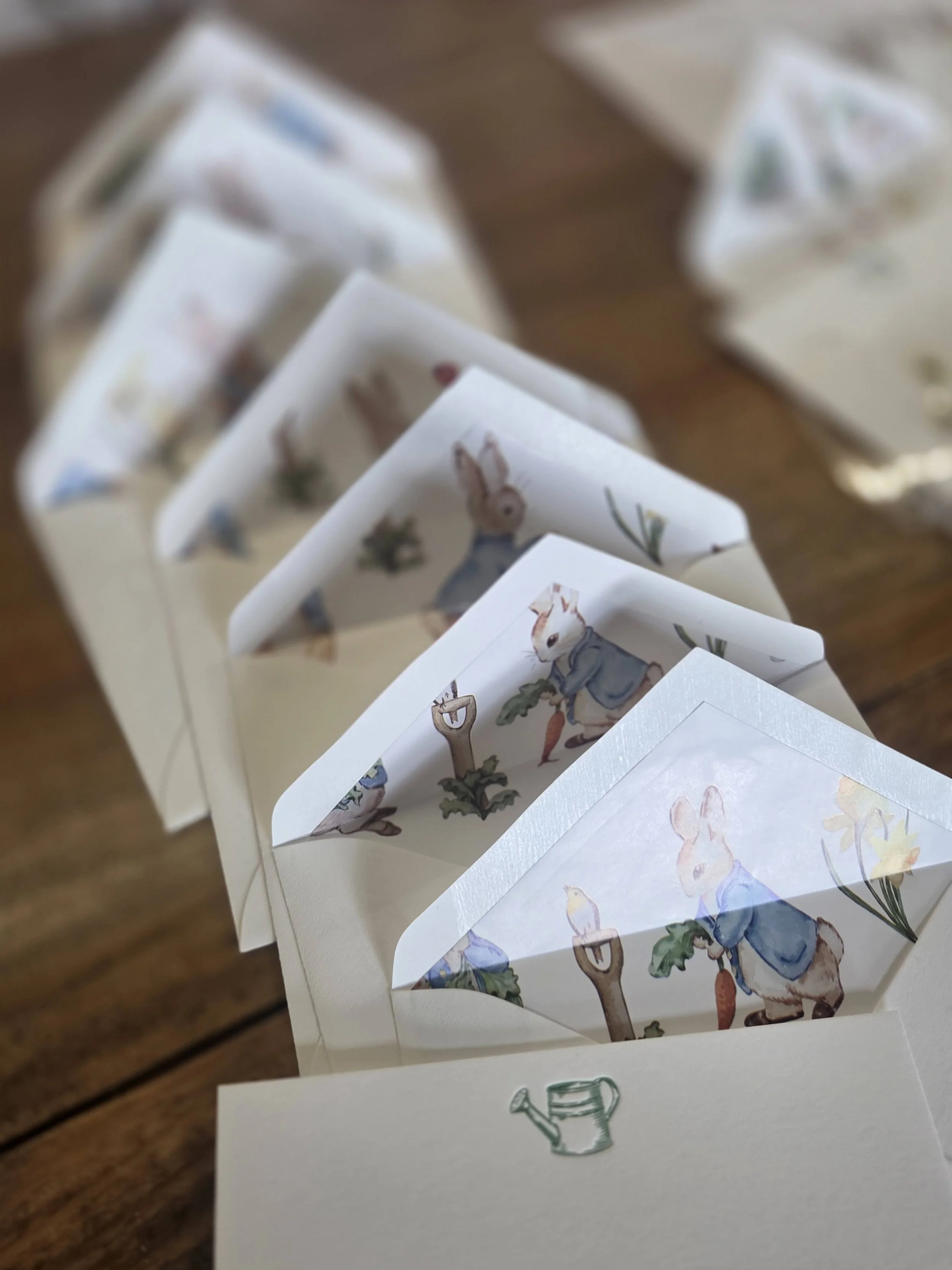 Close-up of a paper booklet with illustrated rabbits and watering cans, arranged on a wooden surface.