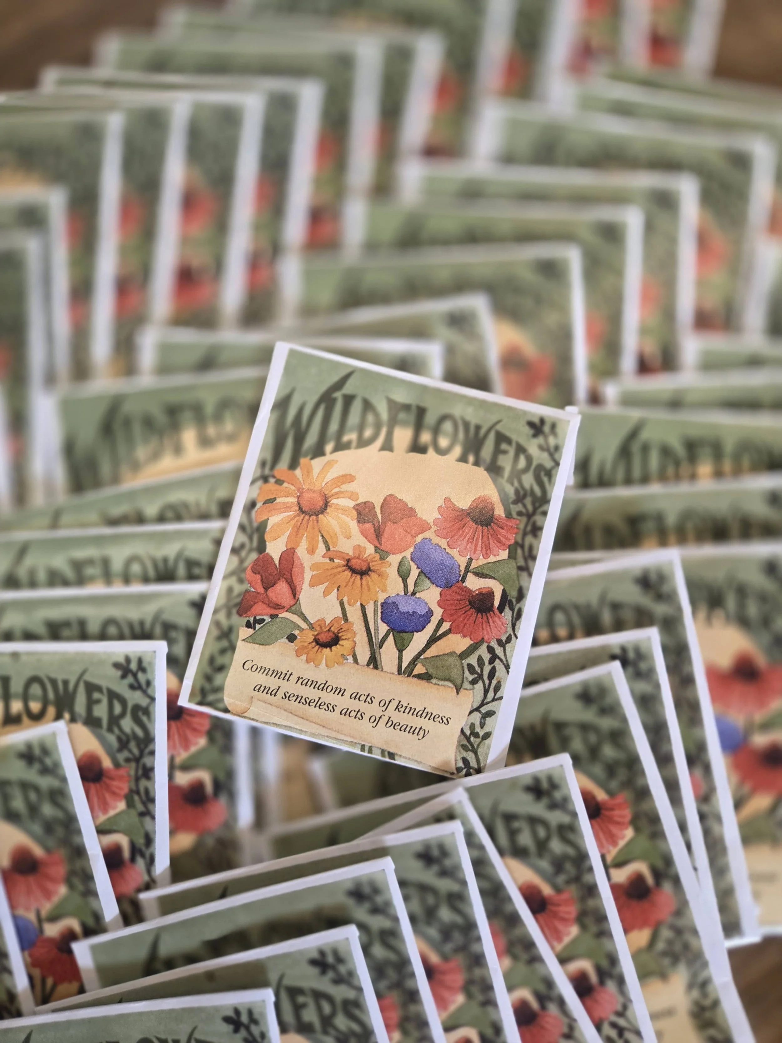 Multiple seed packets labeled 'Wildflower' featuring colorful illustrations of wildflowers with the motto 'commit random acts of kindness and senseless acts of beauty'.