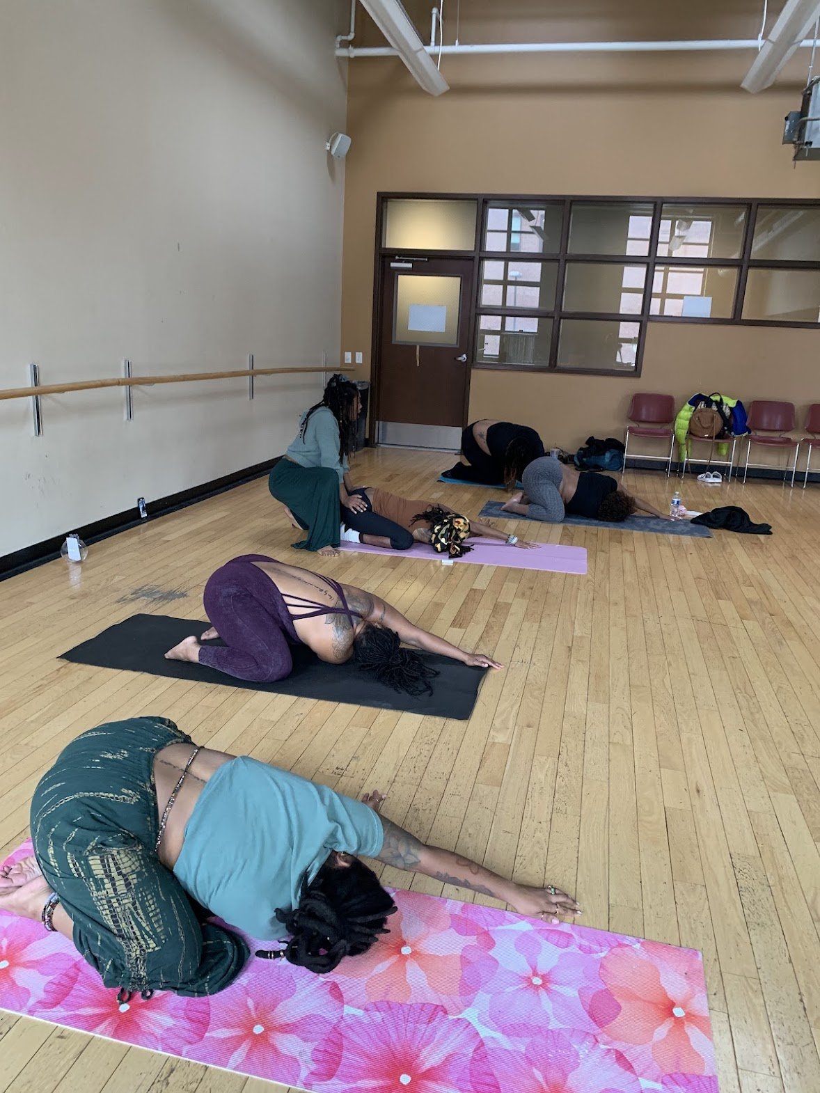 People participating in a yoga class, performing downward dog poses on yoga mats in a spacious indoor studio with wooden floors.