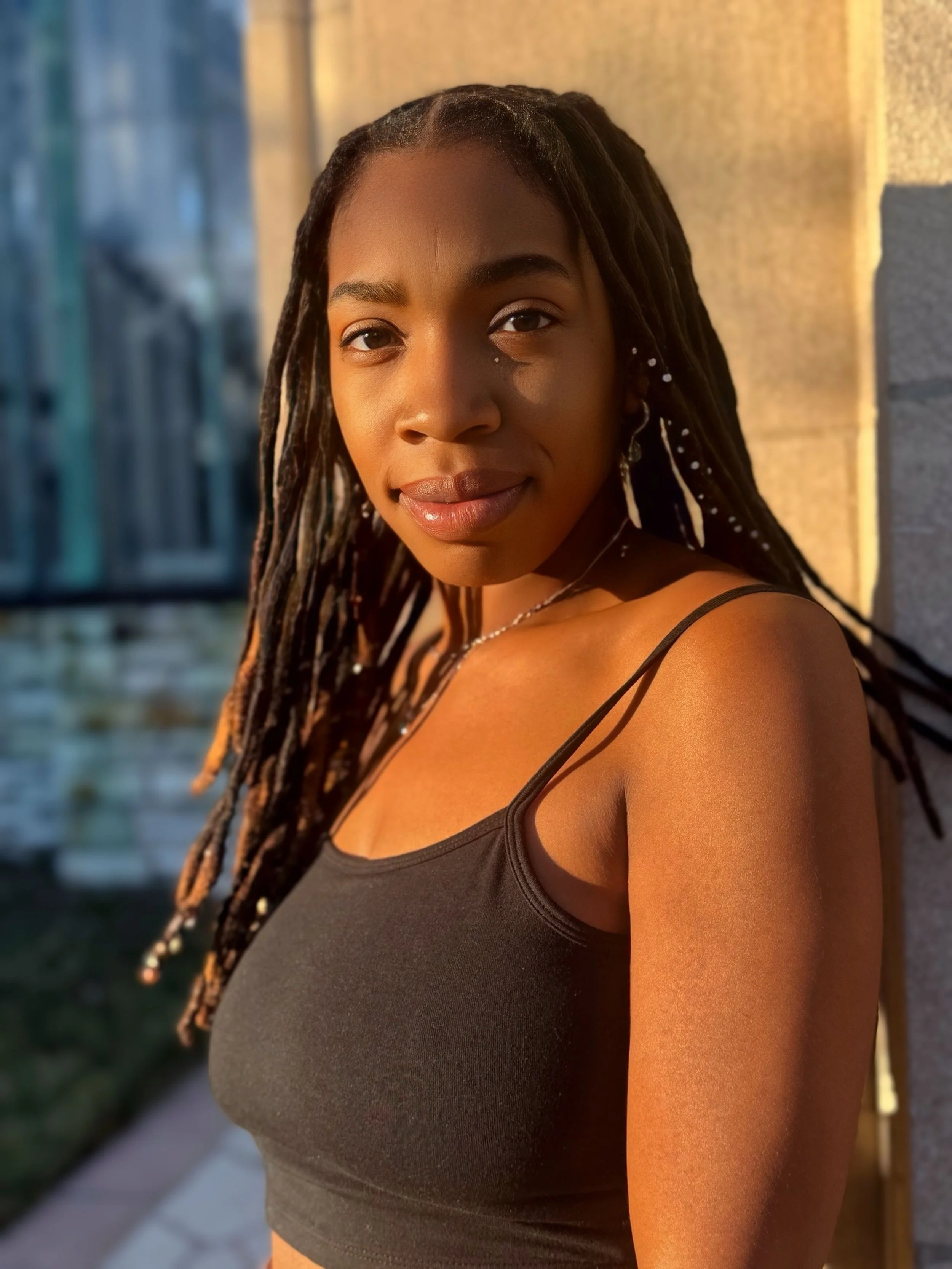 A young woman with long braided hair standing outdoors during sunset.