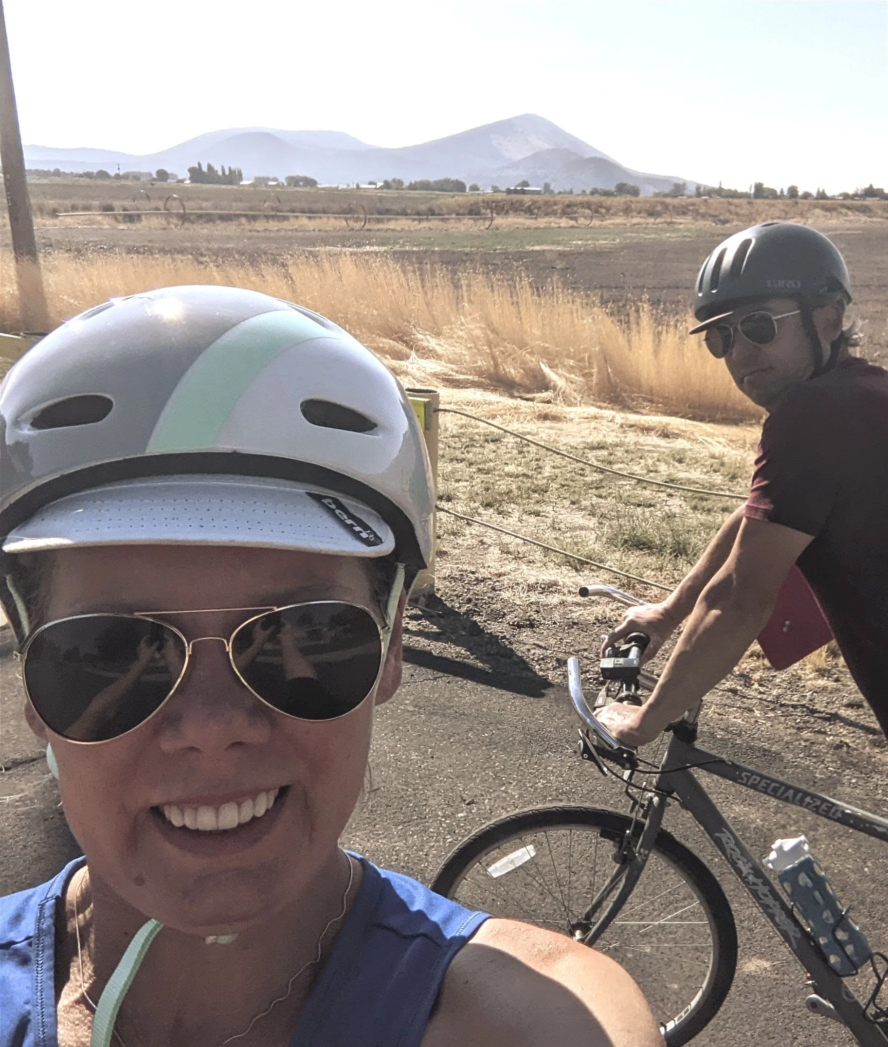 Gretchen Palmer, woman with bike helmet on smiling and her husband on a bike behind her