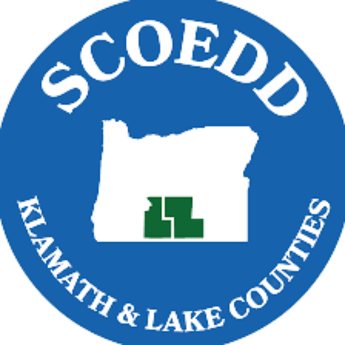 Seal of Skamania County in Washington featuring a white outline of the county, a green tree symbol, and the words "SCOEDD" and "Klamath & Lake Counties".