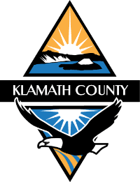 Klamath County logo featuring a rising sun, mountain, water, and two hands holding a star.