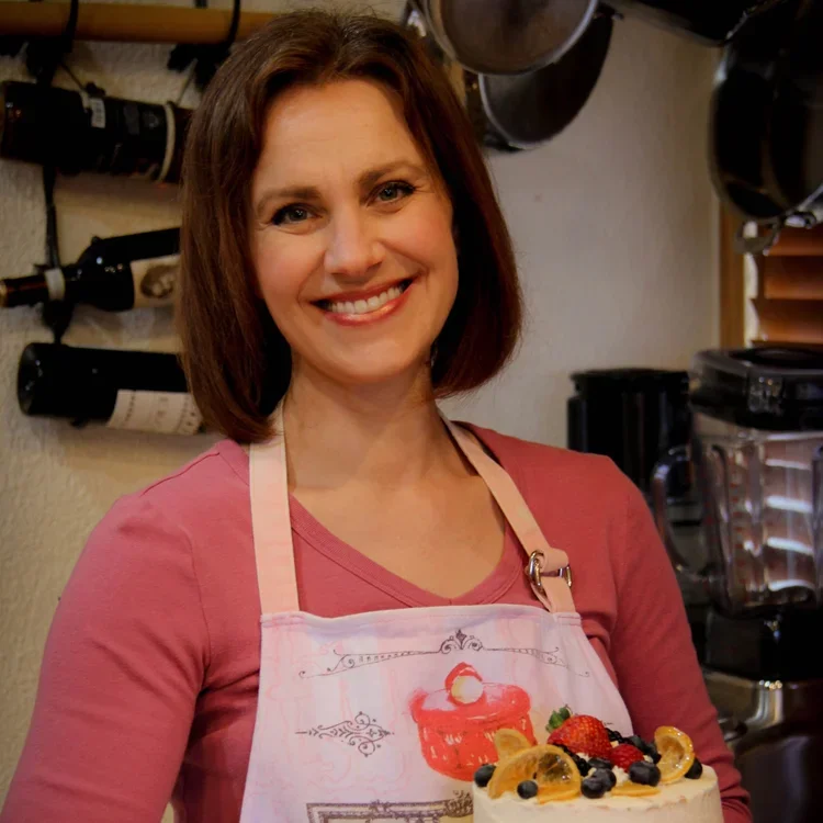 Woman holding a decorated cake in a kitchen.