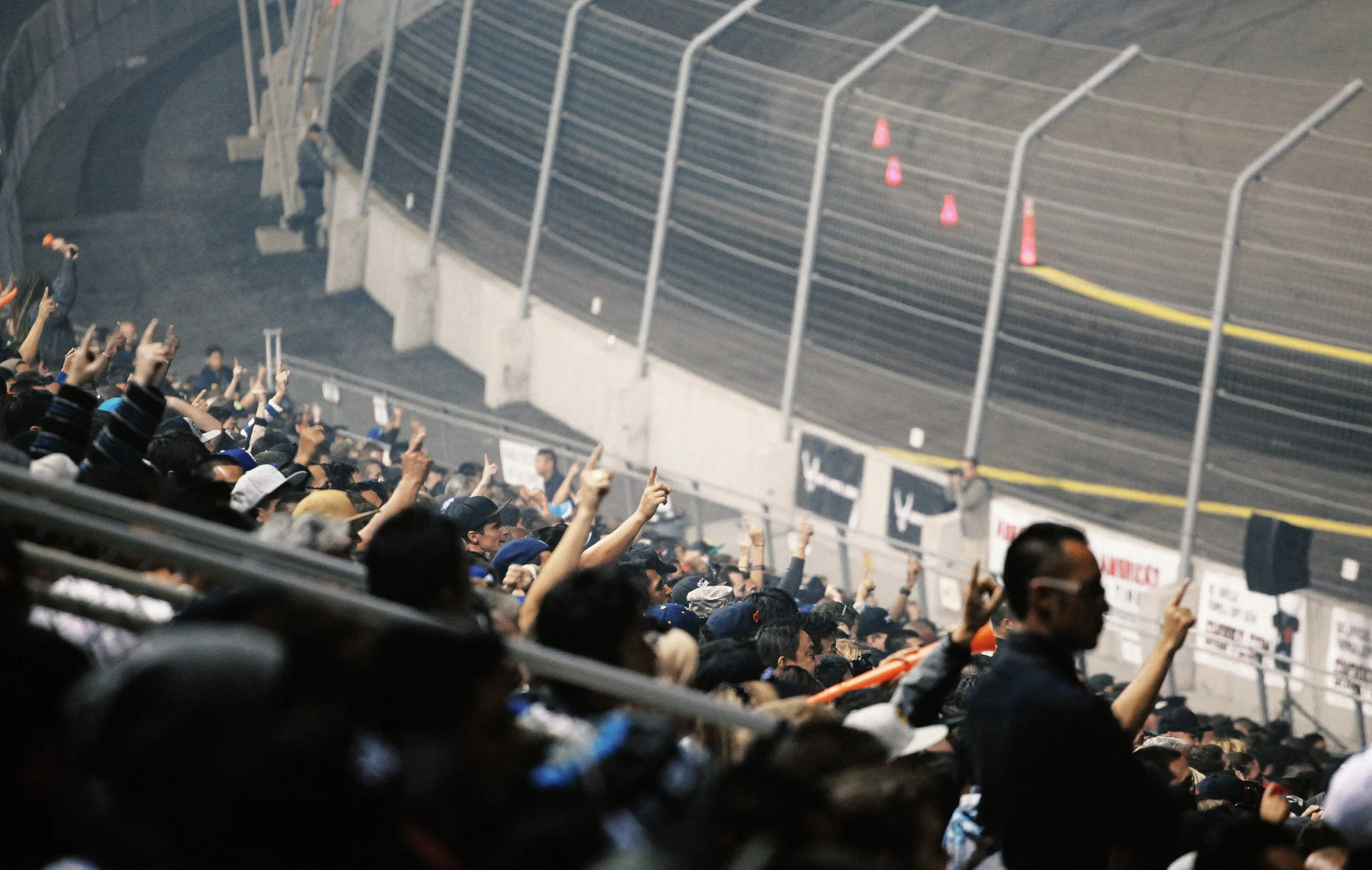 Crowd of people at a racing event pointing towards a section of the track with traffic cones and barriers.