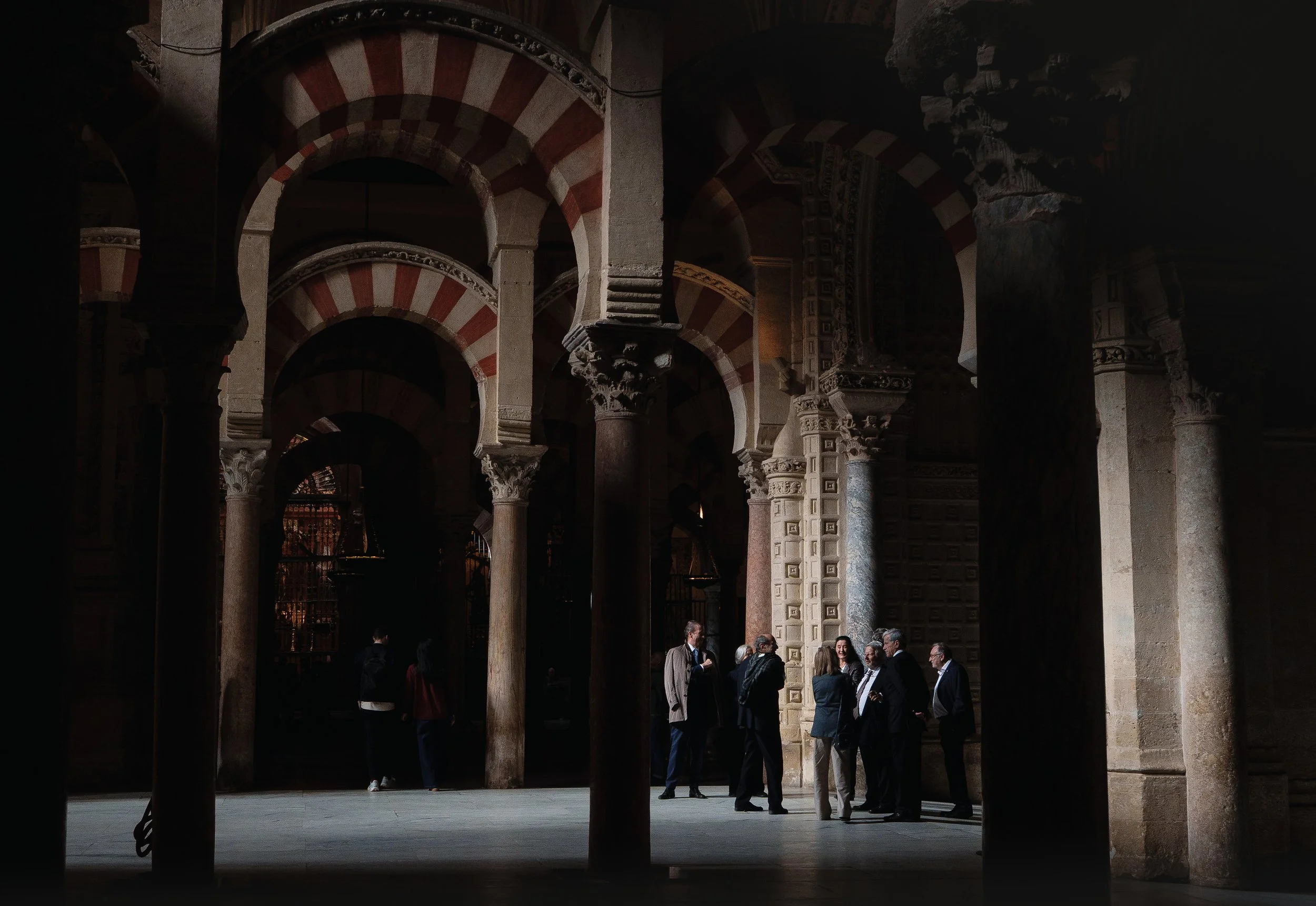 Group of people standing and talking inside an old historic building with arches and columns.