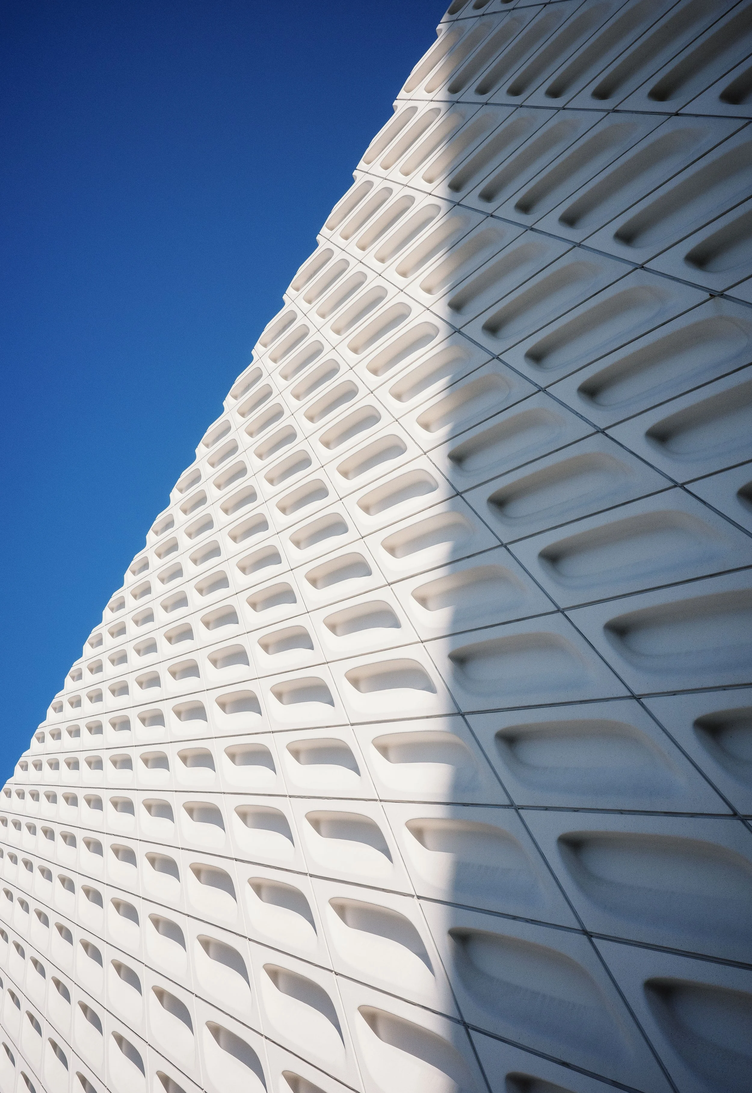 Close-up view of a modern architectural building with a white, geometric, patterned facade against a clear blue sky.